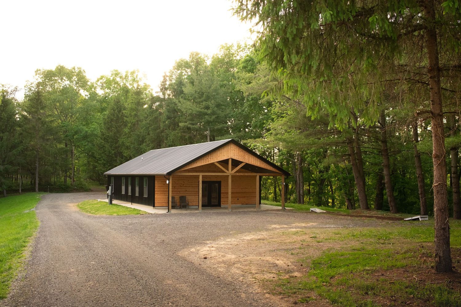 Rustic wooden cabin with gravel driveway nestled among pine trees at sunset.