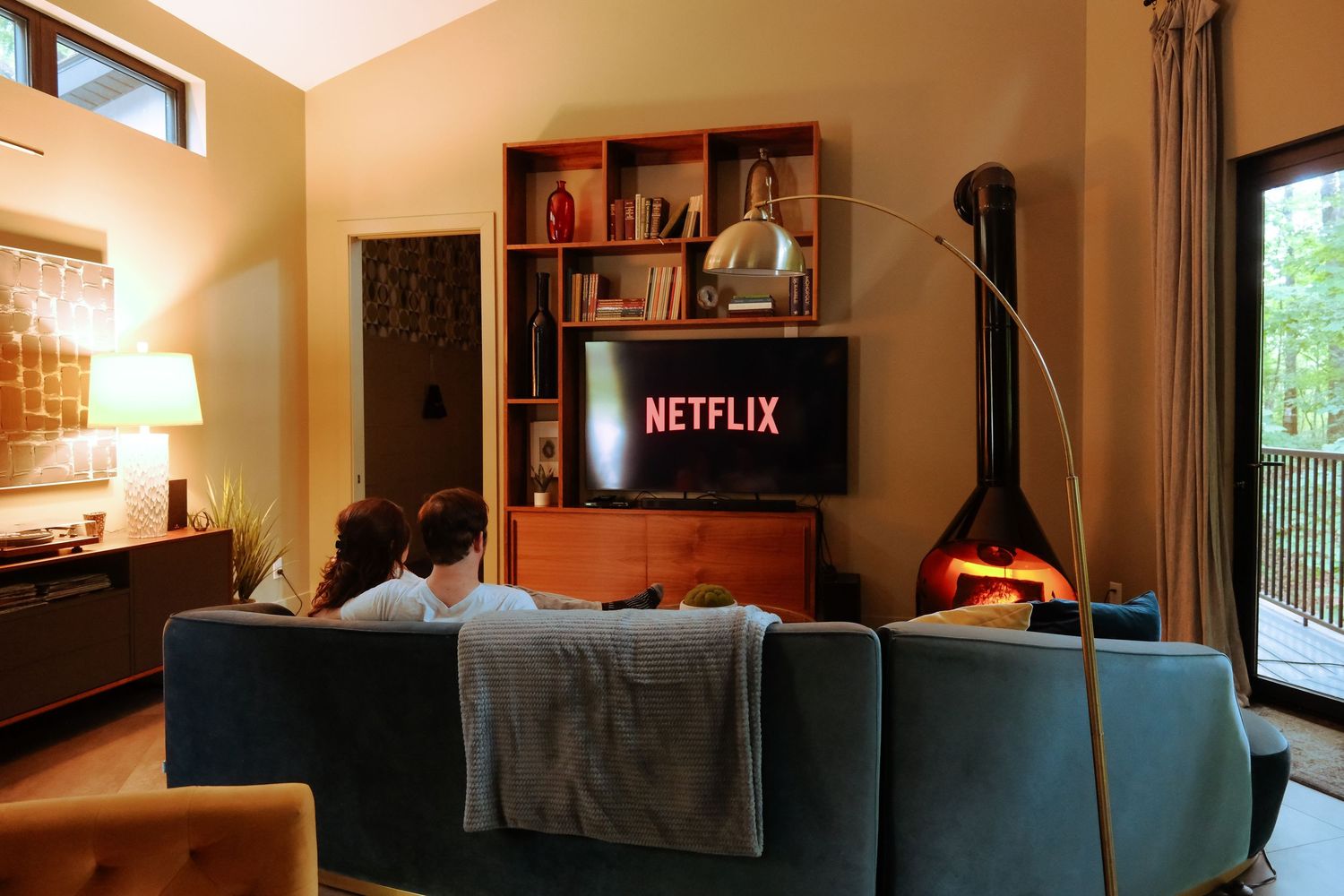 Person watching Netflix on a large TV in a cozy modern living room with a fireplace and bookshelf.