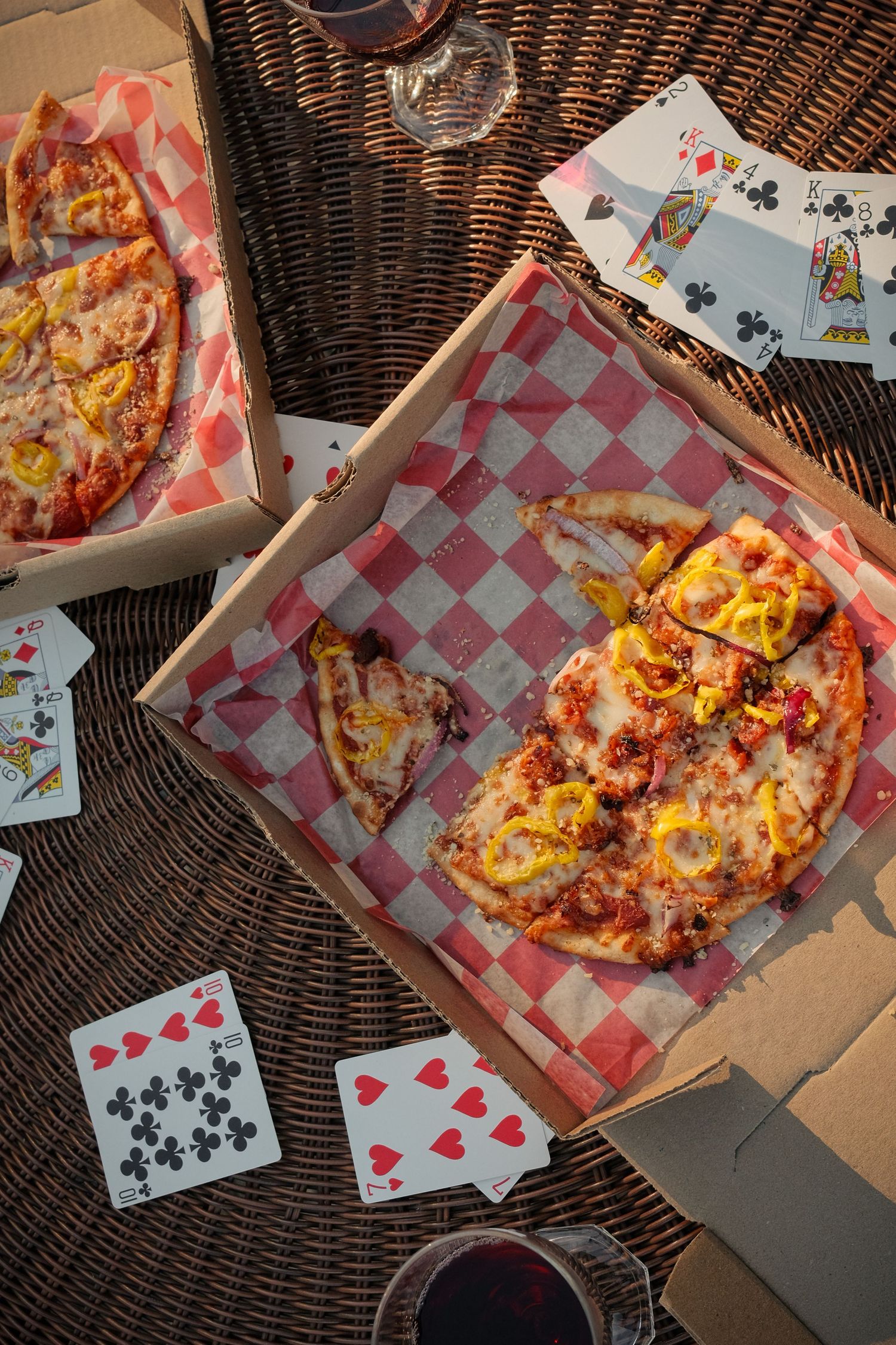 Pizza and playing cards laid out on wicker furniture for a casual game night.