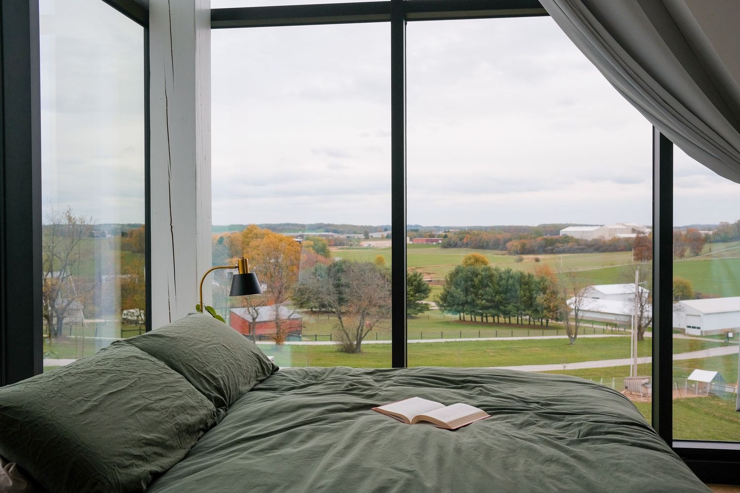 Scenic fall countryside vista seen through large modern windows with bed in foreground.