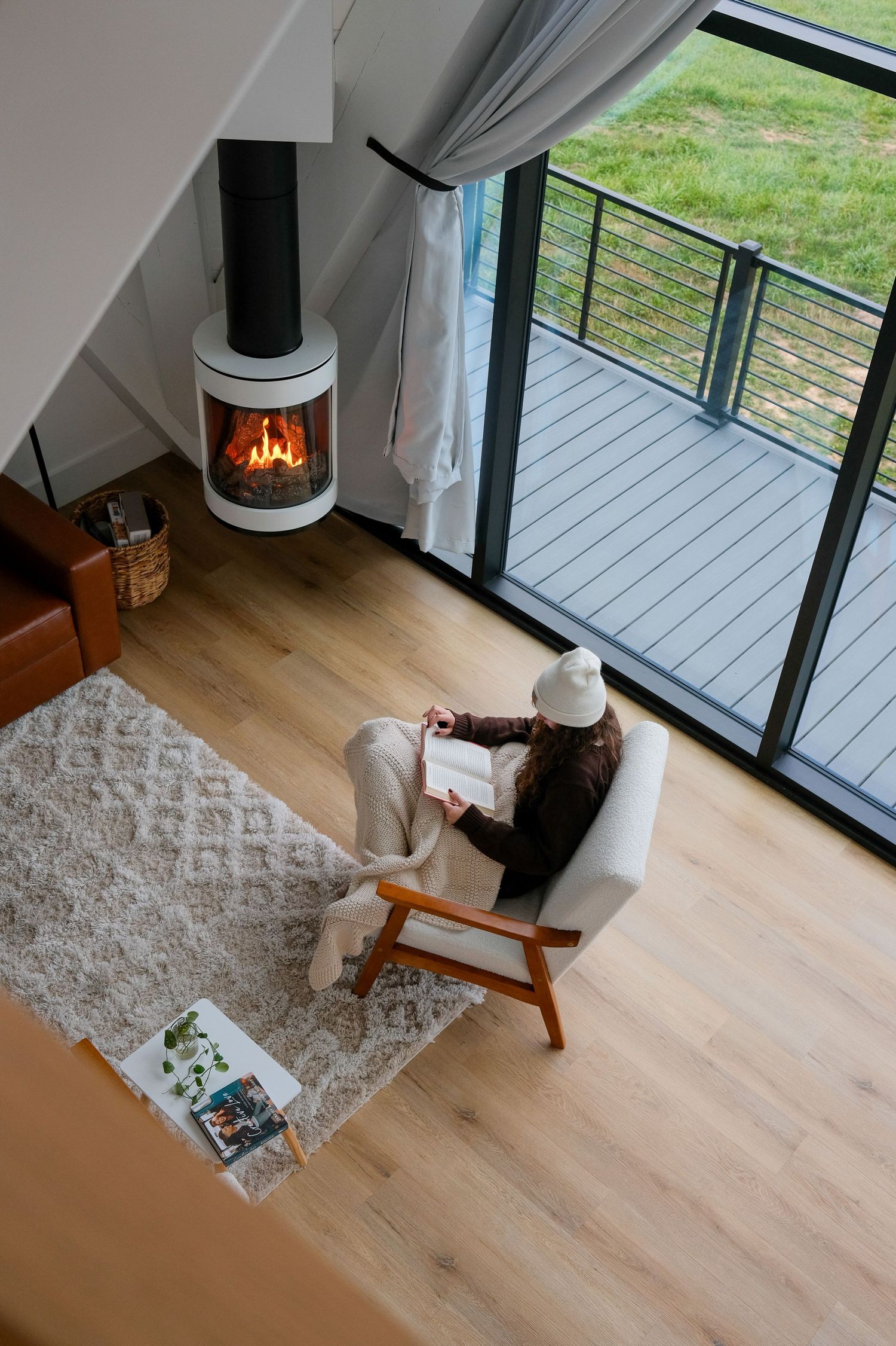 Modern living room with wood floors, fireplace, and large windows overlooking outdoor deck.