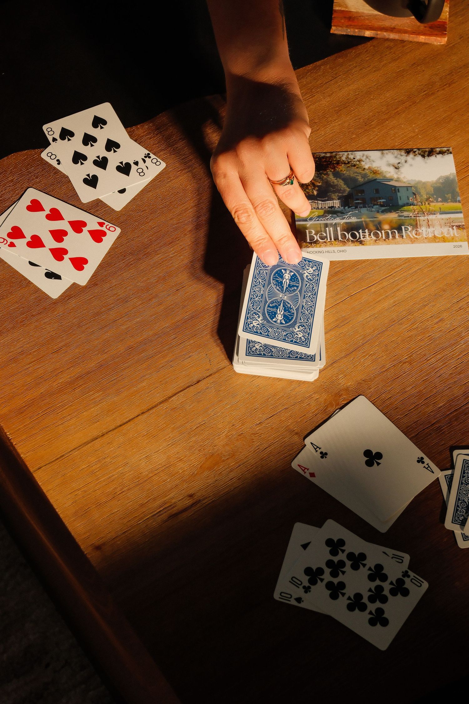 Hand holding a deck of Bicycle playing cards on a wooden table with scattered cards during a card game.