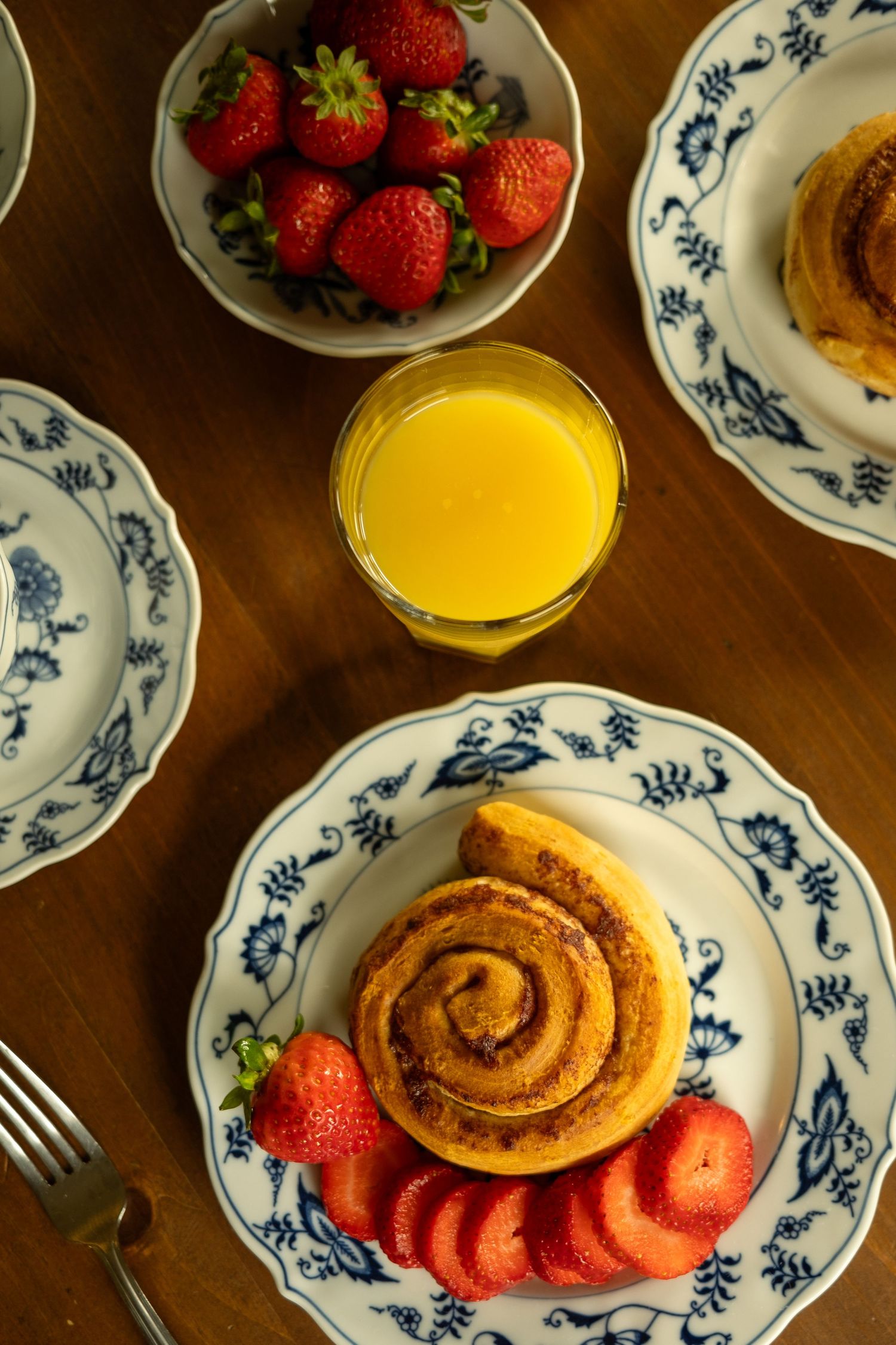 Fresh strawberries and cinnamon rolls served on blue and white patterned plates with orange juice.