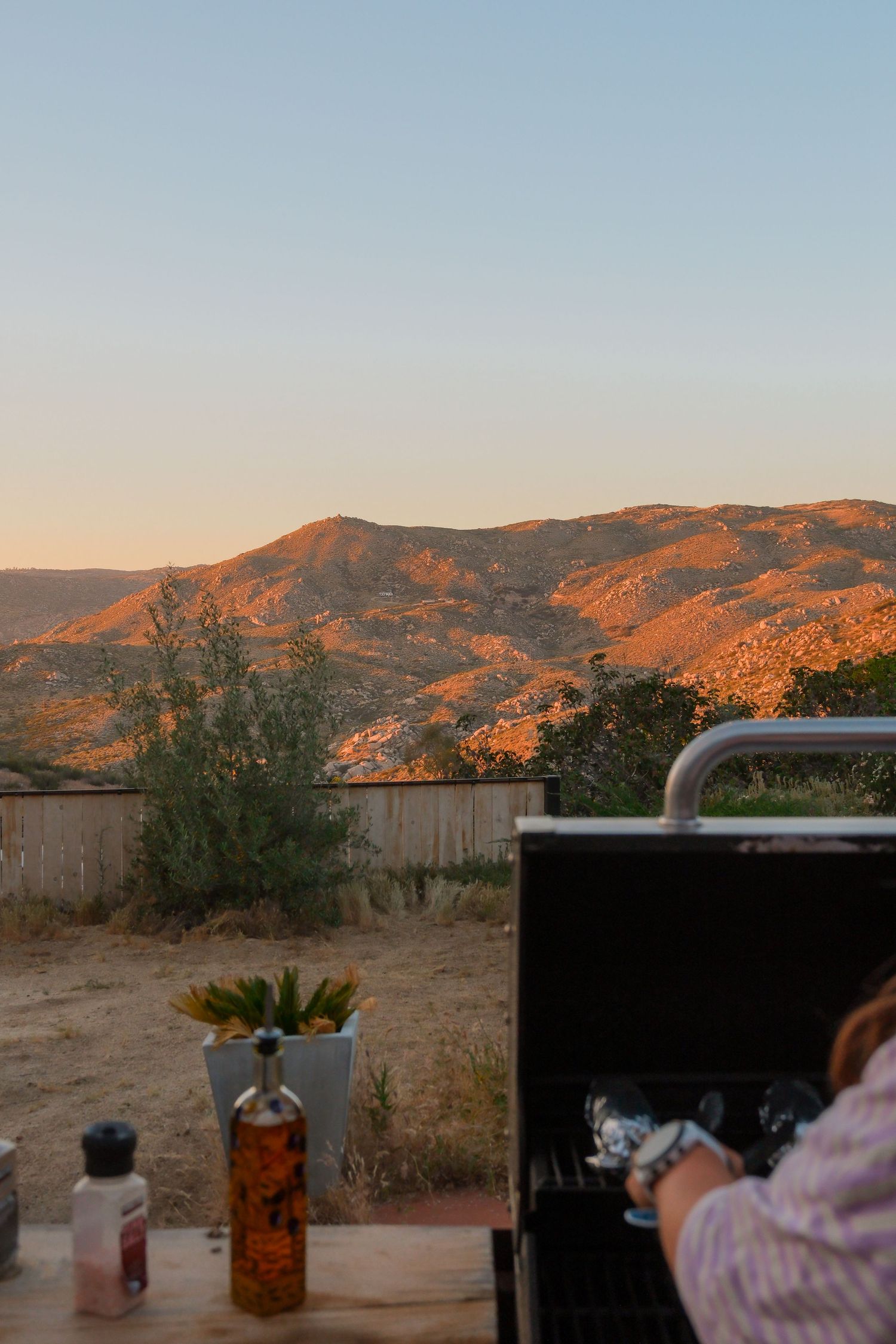 Woman grilling at outdoor BBQ with breathtaking golden sunset mountain landscape views in the background.