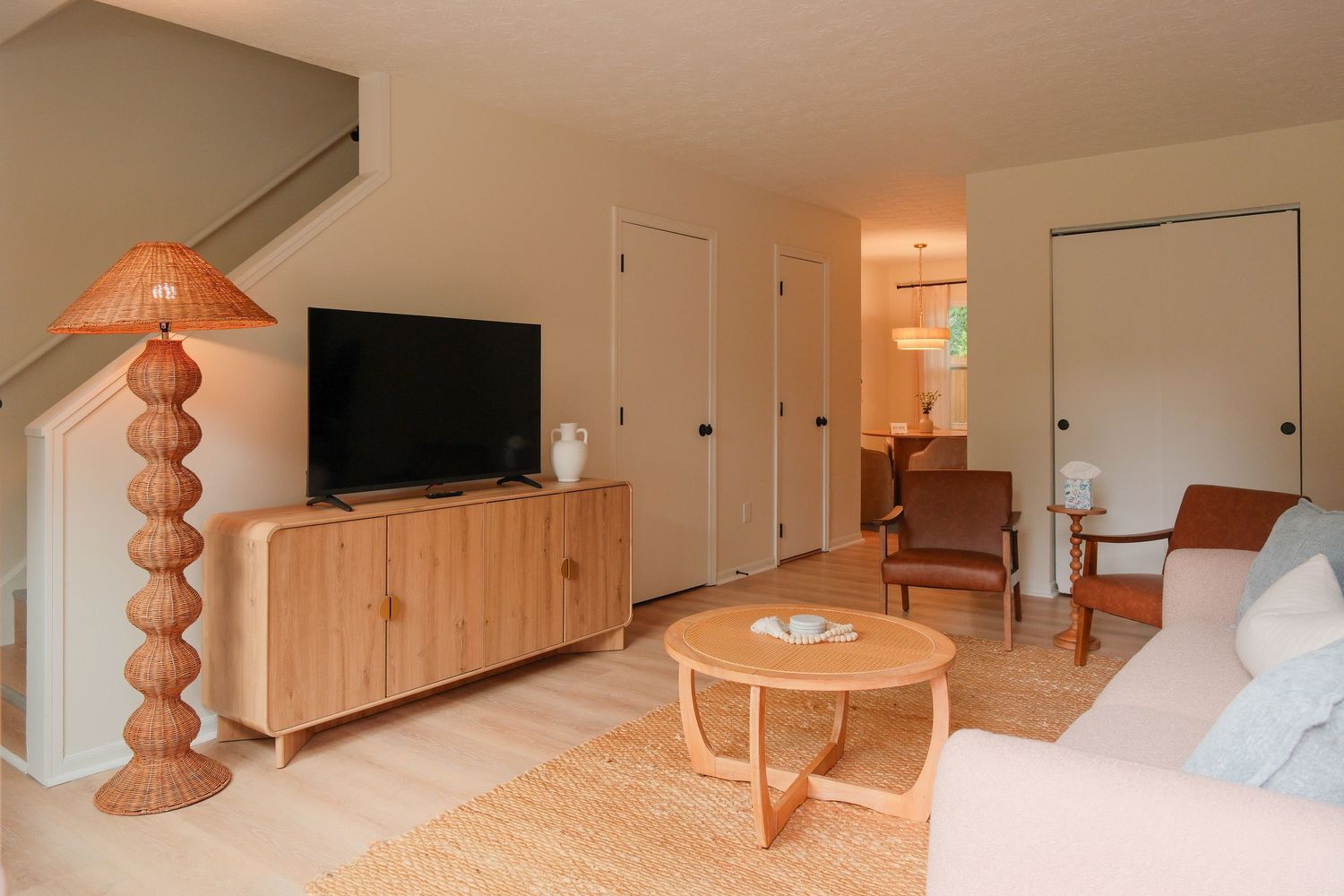 Cozy living room with light wood TV console, rattan floor lamp, round coffee table, and neutral tones creating a warm, modern space.