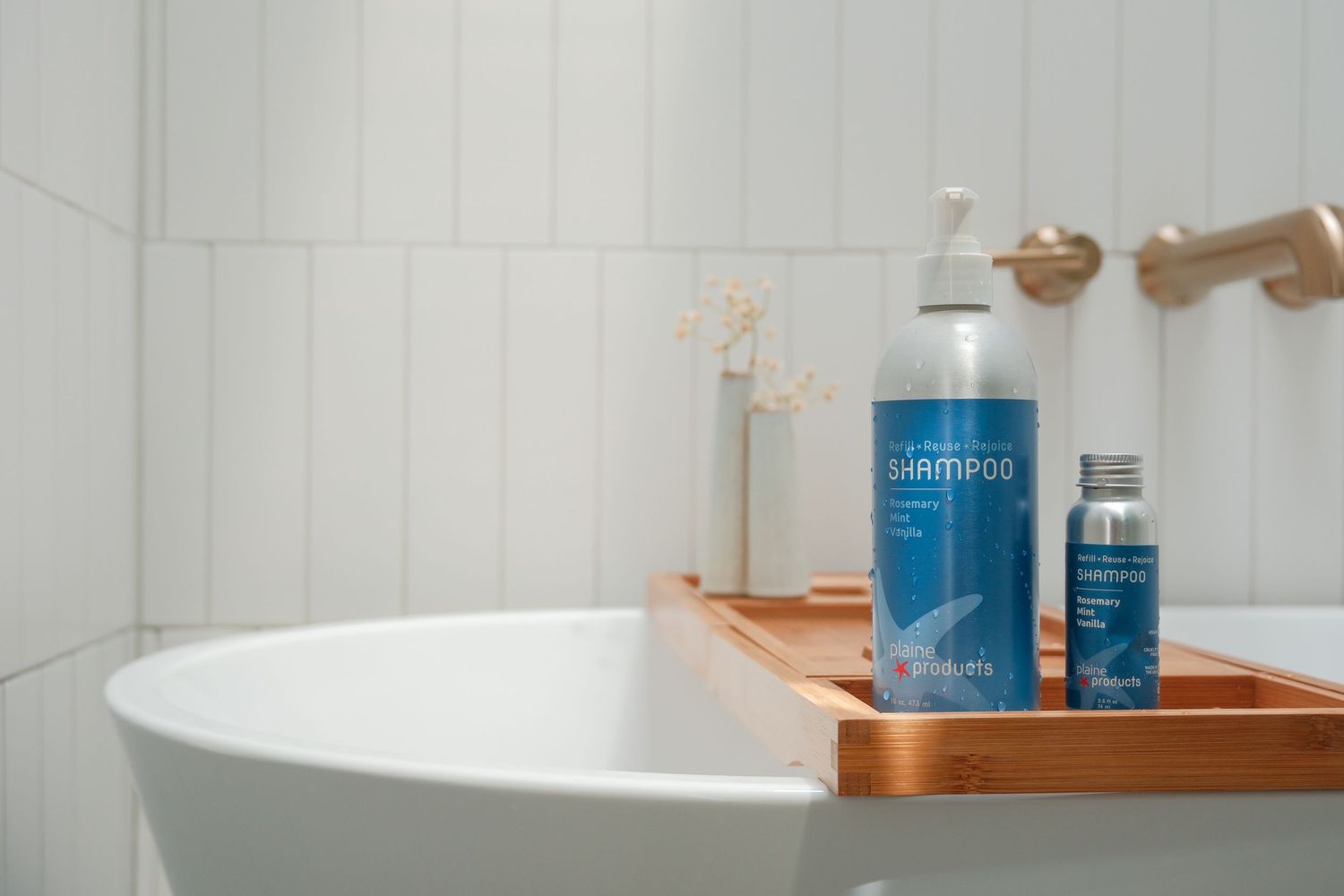 Two blue shampoo bottles on a wooden bath tray beside a white bathtub in a modern bathroom.