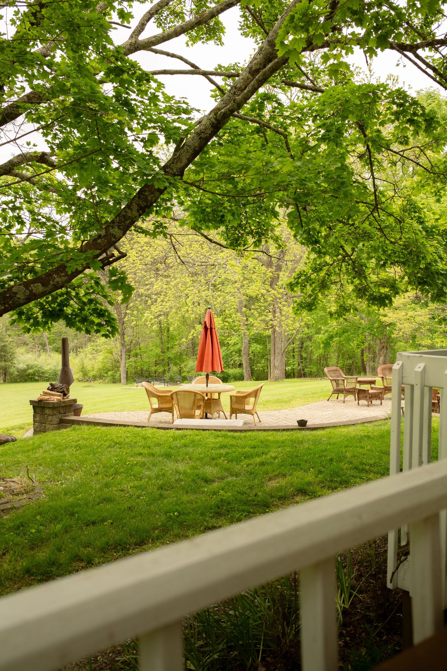Green lawn with mature trees and outdoor seating viewed through porch railing.