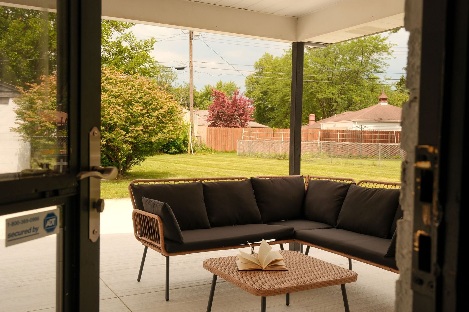 Screened porch with dark sectional sofa and wood coffee table overlooking a lush green backyard.