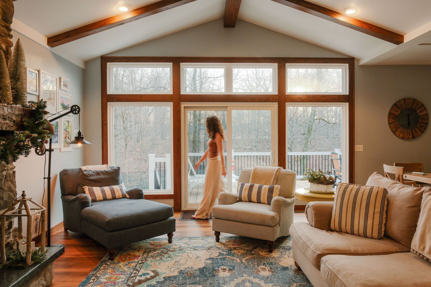 Cozy rustic living room with exposed wooden beams, warm lighting, and comfortable seating arranged around large windows.