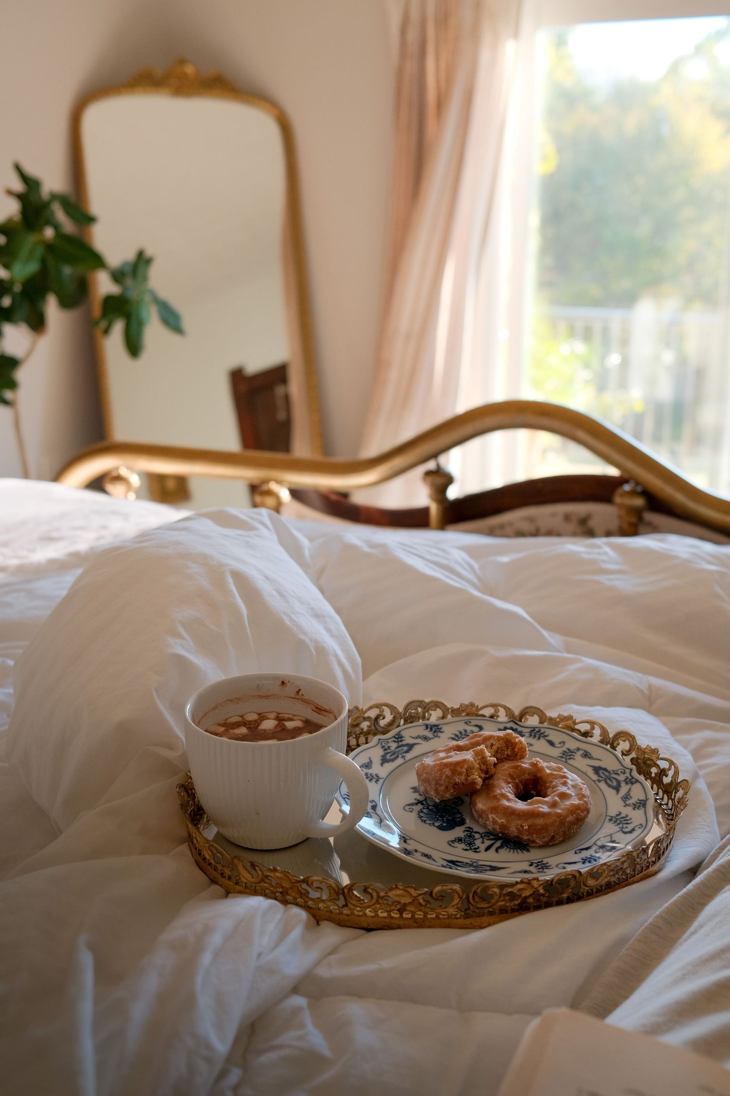 Breakfast tray with pastries on white bedding in natural sunlight.