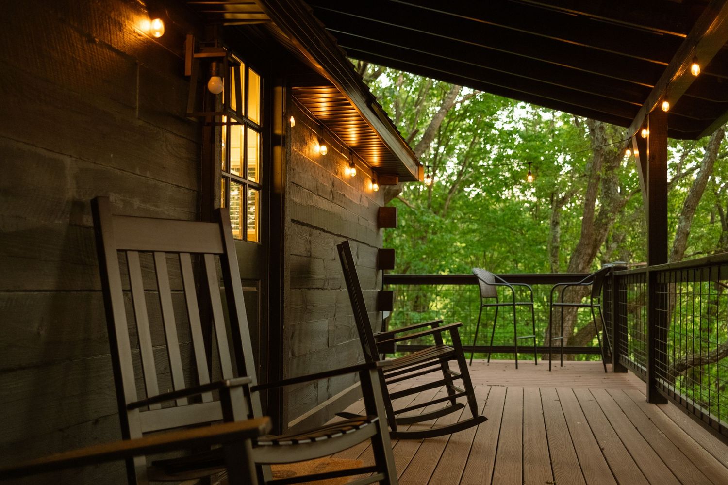 Covered wooden deck with rocking chairs and string lights creating a warm ambiance.