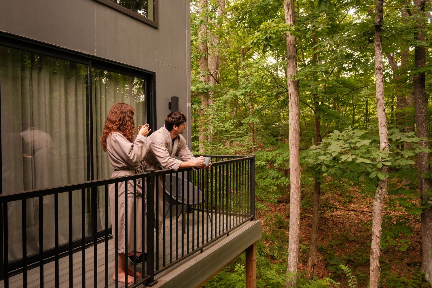 Two guests in robes enjoy a wooded balcony view at a luxury forest retreat.
