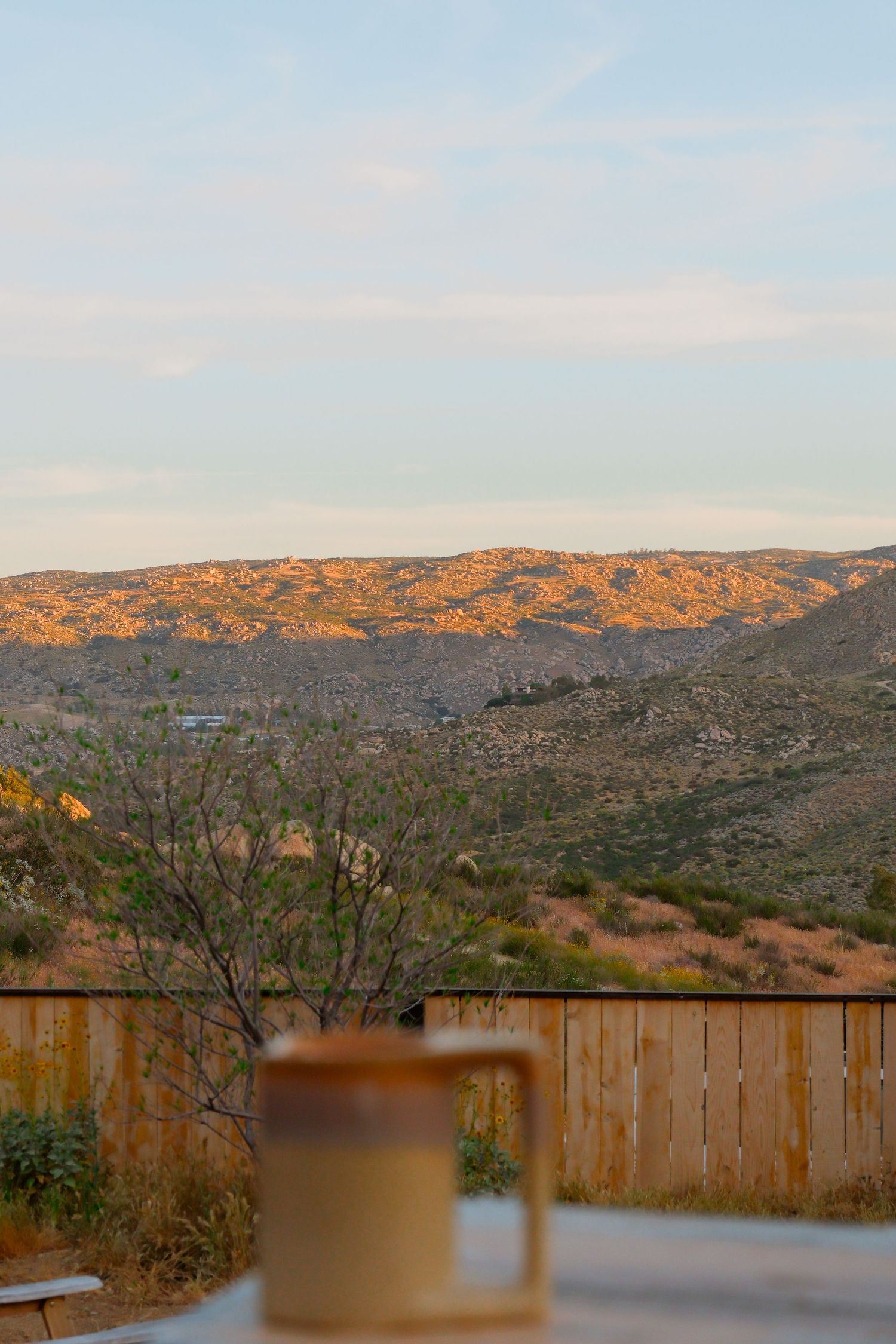 A ceramic mug on a deck railing with a stunning golden sunset view of rugged desert hills in the background.