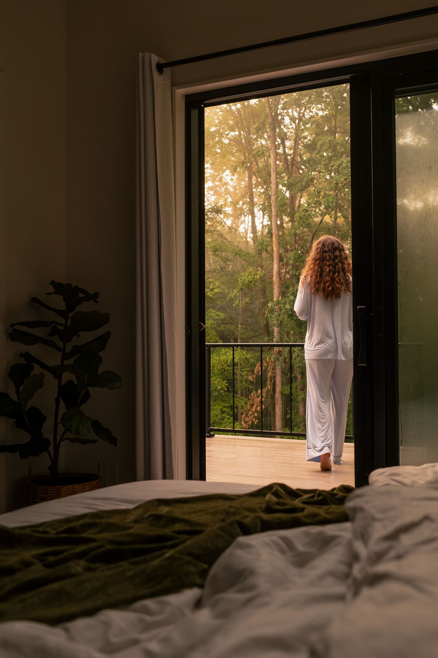 Peaceful bedroom scene with figure standing on balcony overlooking misty forest at sunrise.