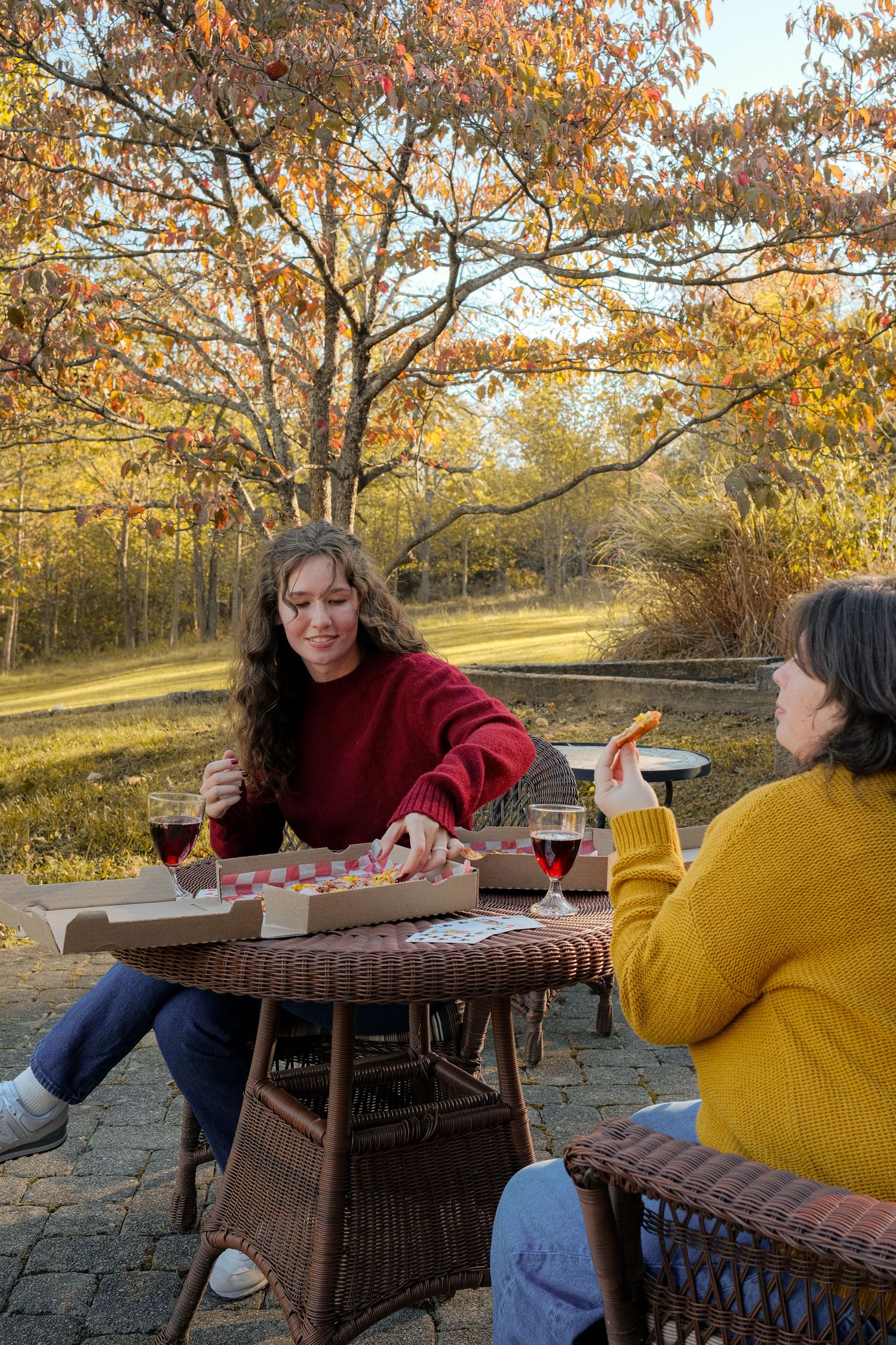 Friends sharing pizza and wine at an outdoor table during autumn sunset.