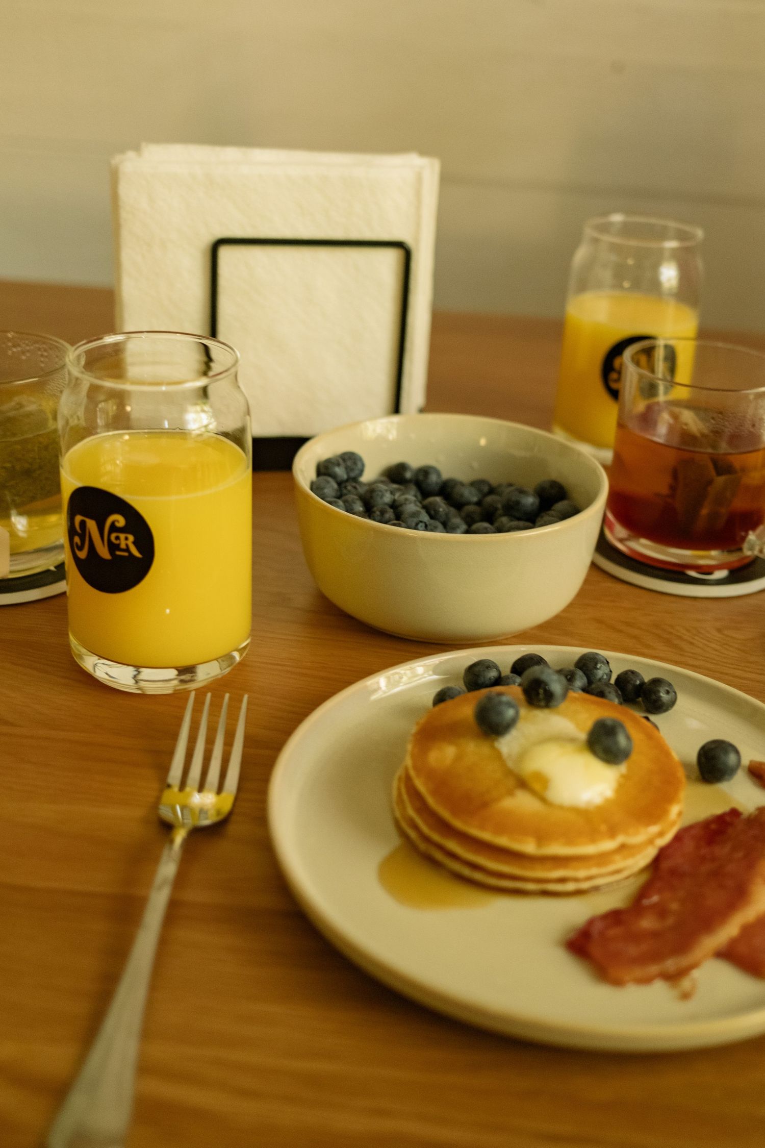 Breakfast spread with pancakes, bacon, blueberries and orange juice on wooden table.