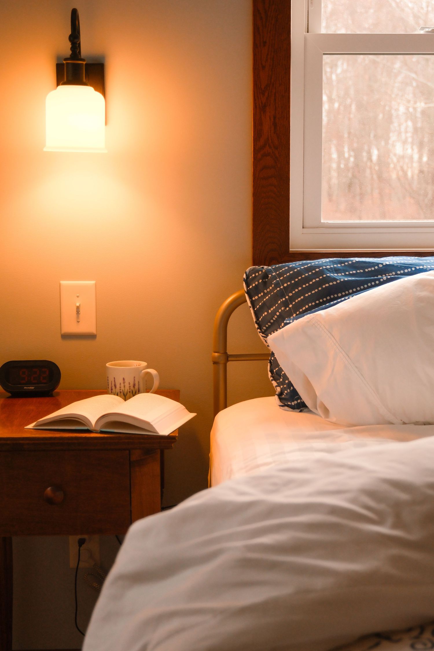 Cozy bedroom interior with warm lighting, white bedding, and an open book on the nightstand.