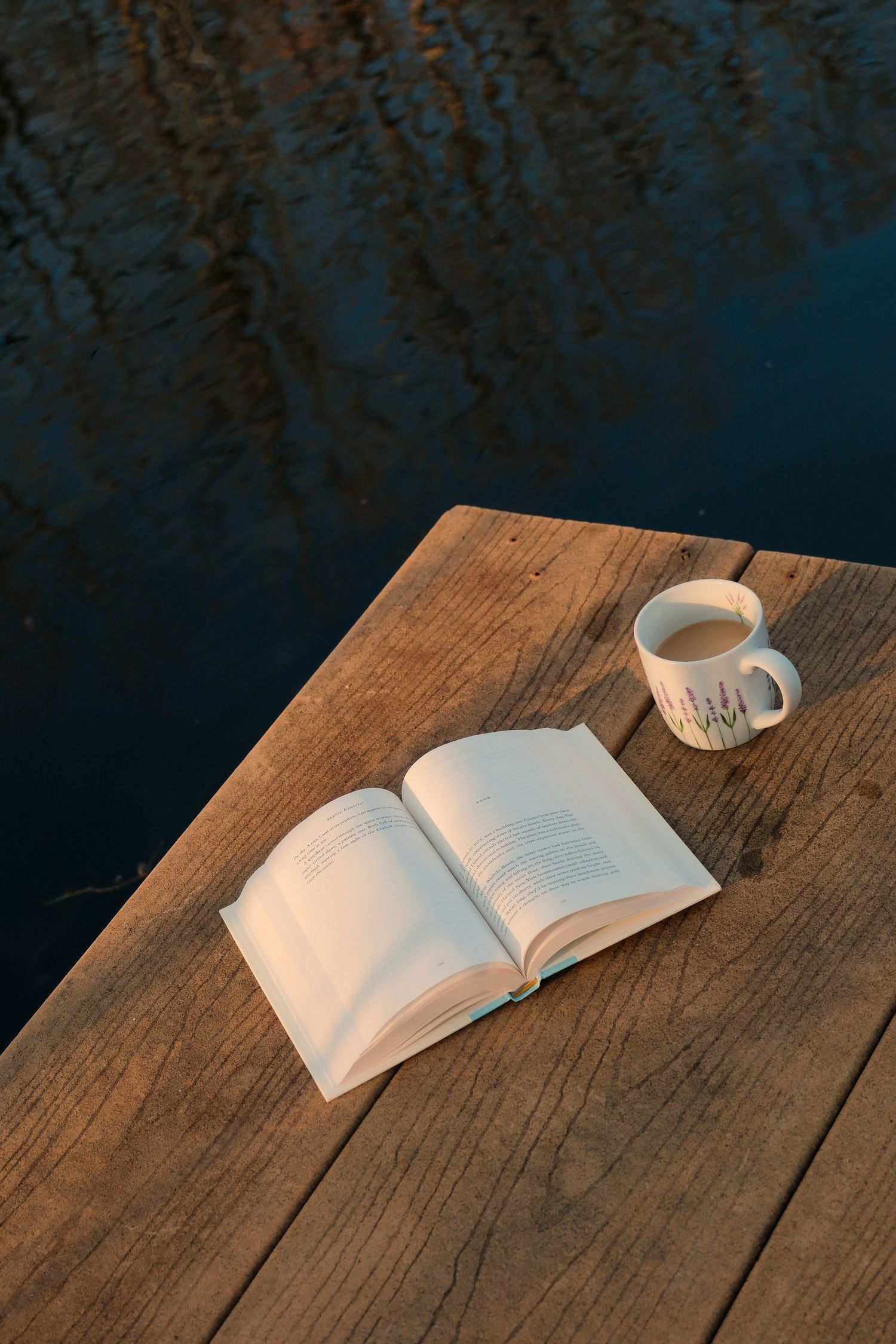 An open book and white coffee cup sit on a rustic wooden table in moody lighting.