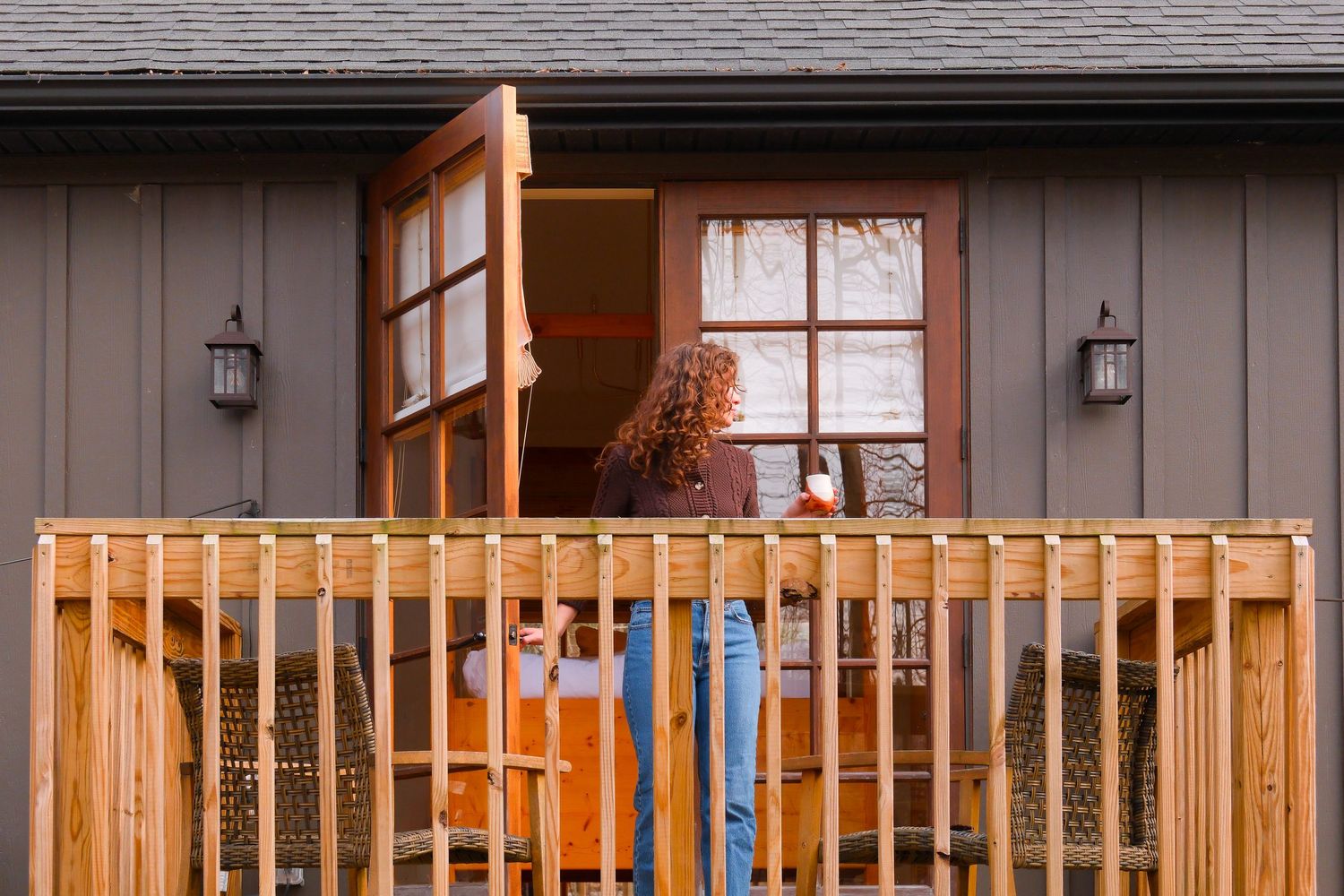 Woman with curly hair opening a wooden door on a newly built cedar deck with white railing.