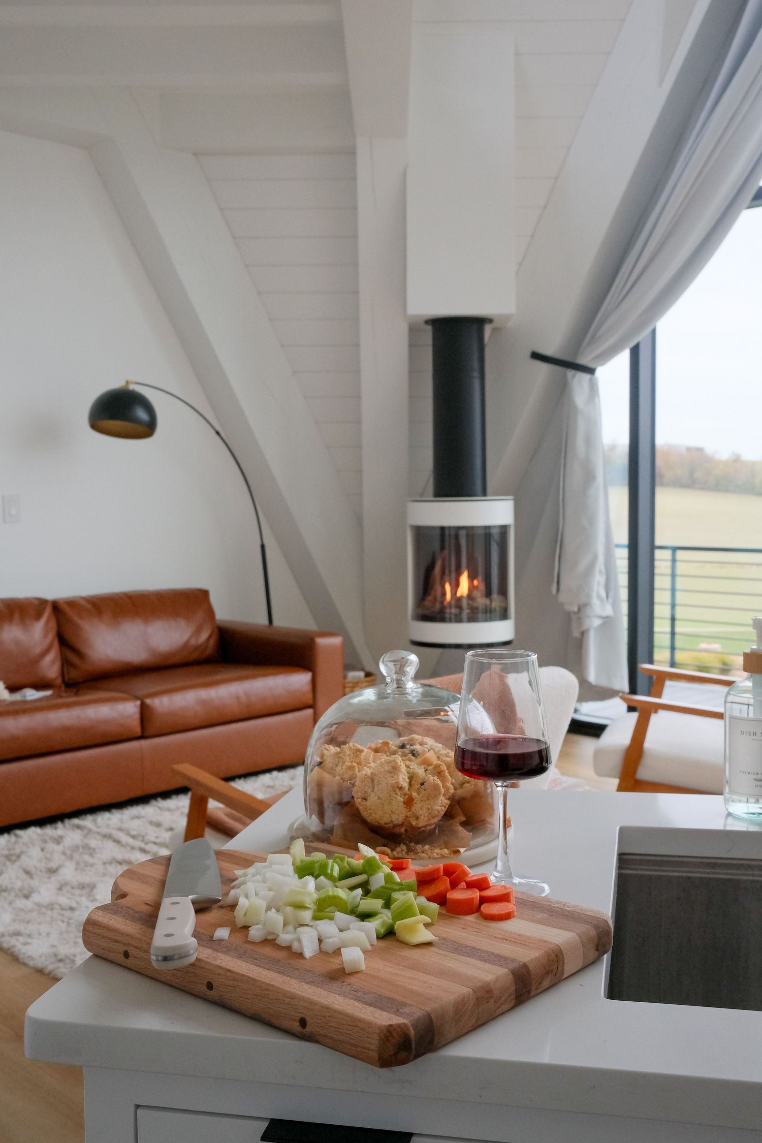 Cozy living space with leather couch, cutting board of vegetables, and wine glass near fireplace.