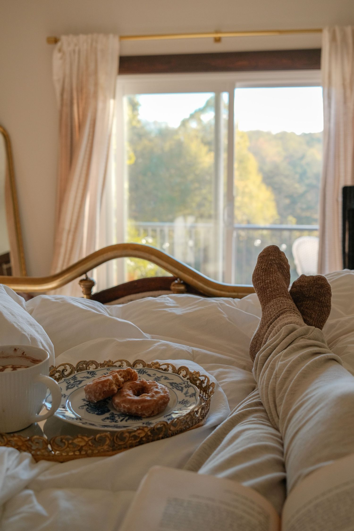 Cozy bedroom view with white bedding and autumn scenery visible through large windows.