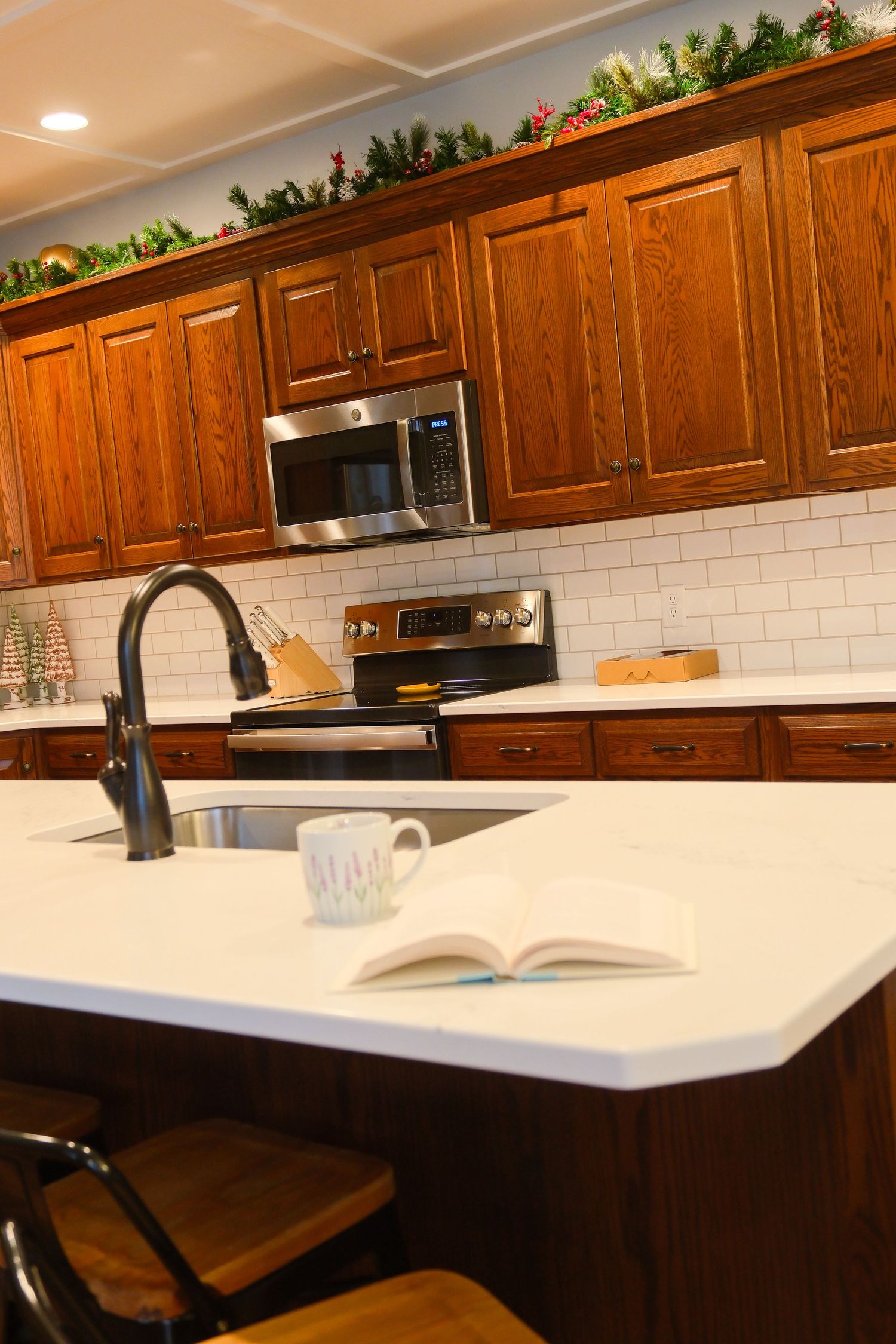 White quartz kitchen counter with wooden cabinets and subway tile backsplash featuring an open book and modern fixtures.