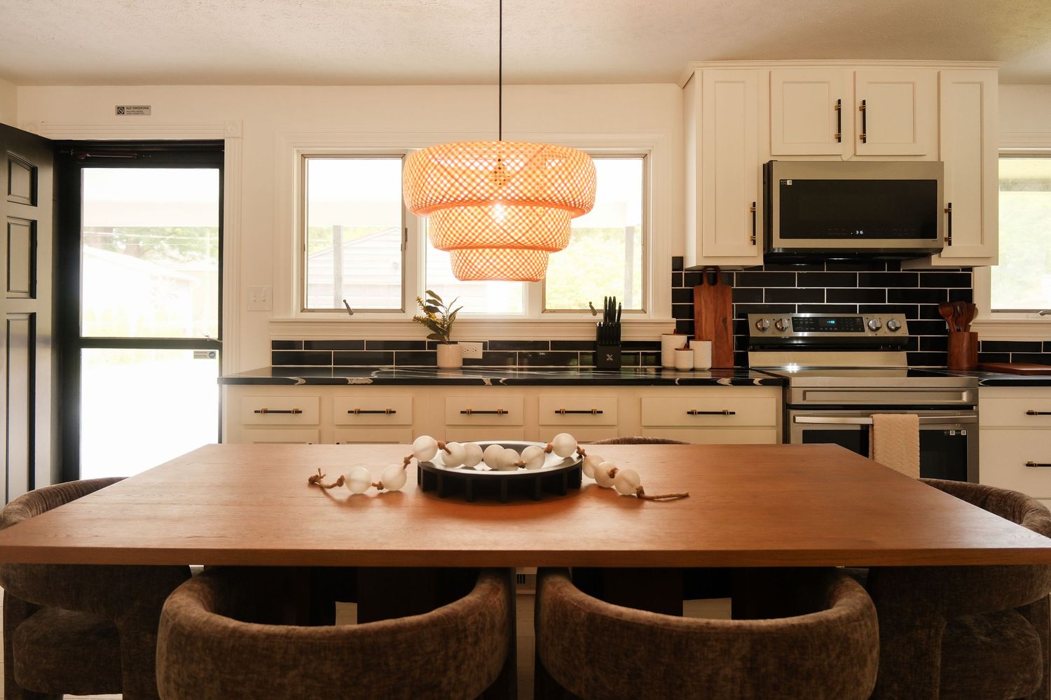 Modern kitchen with white cabinets, black subway tile backsplash, stainless appliances, and a wooden dining table with woven pendant light.