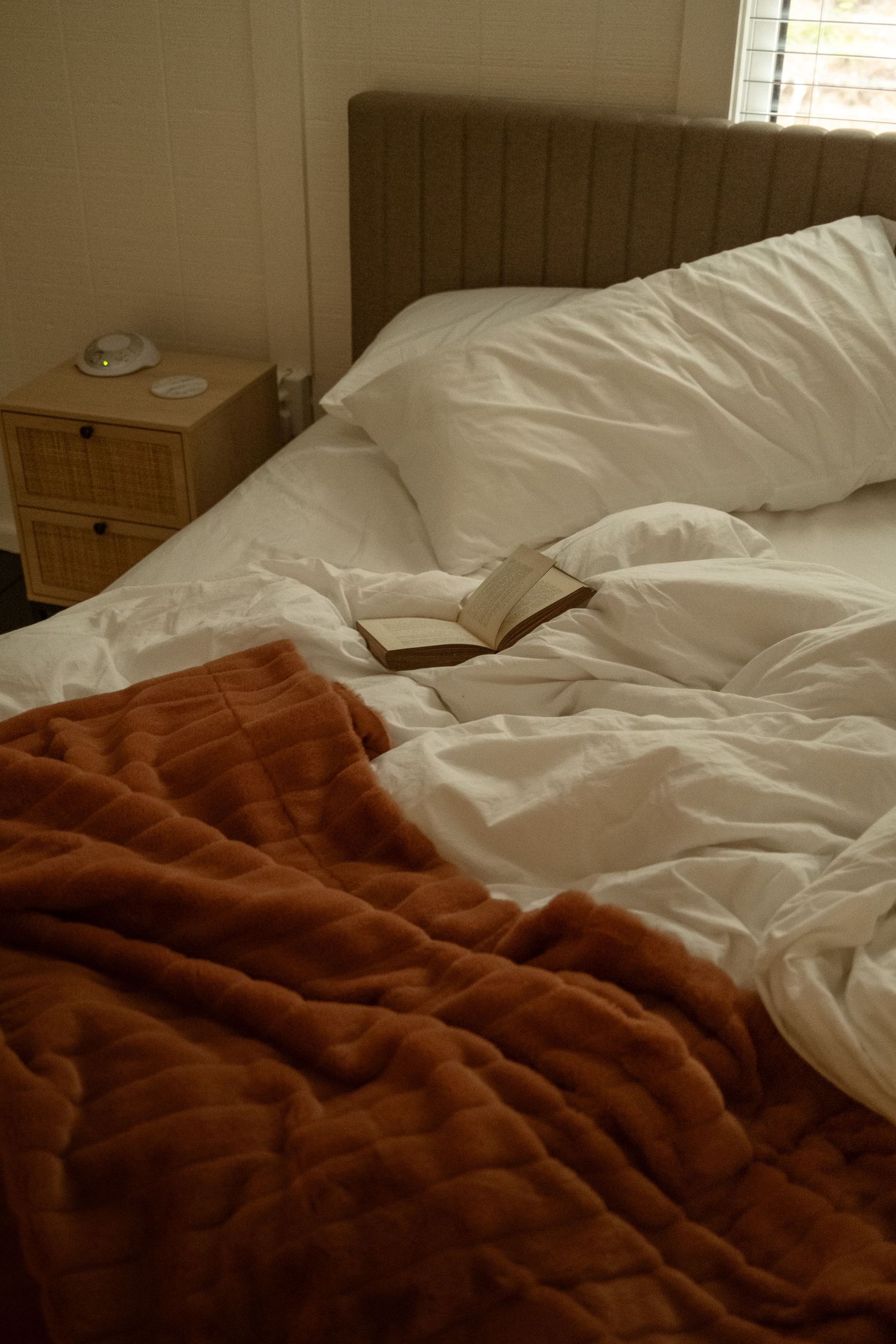 Unmade bed with white sheets and a cozy brown blanket in a rustic bedroom setting.