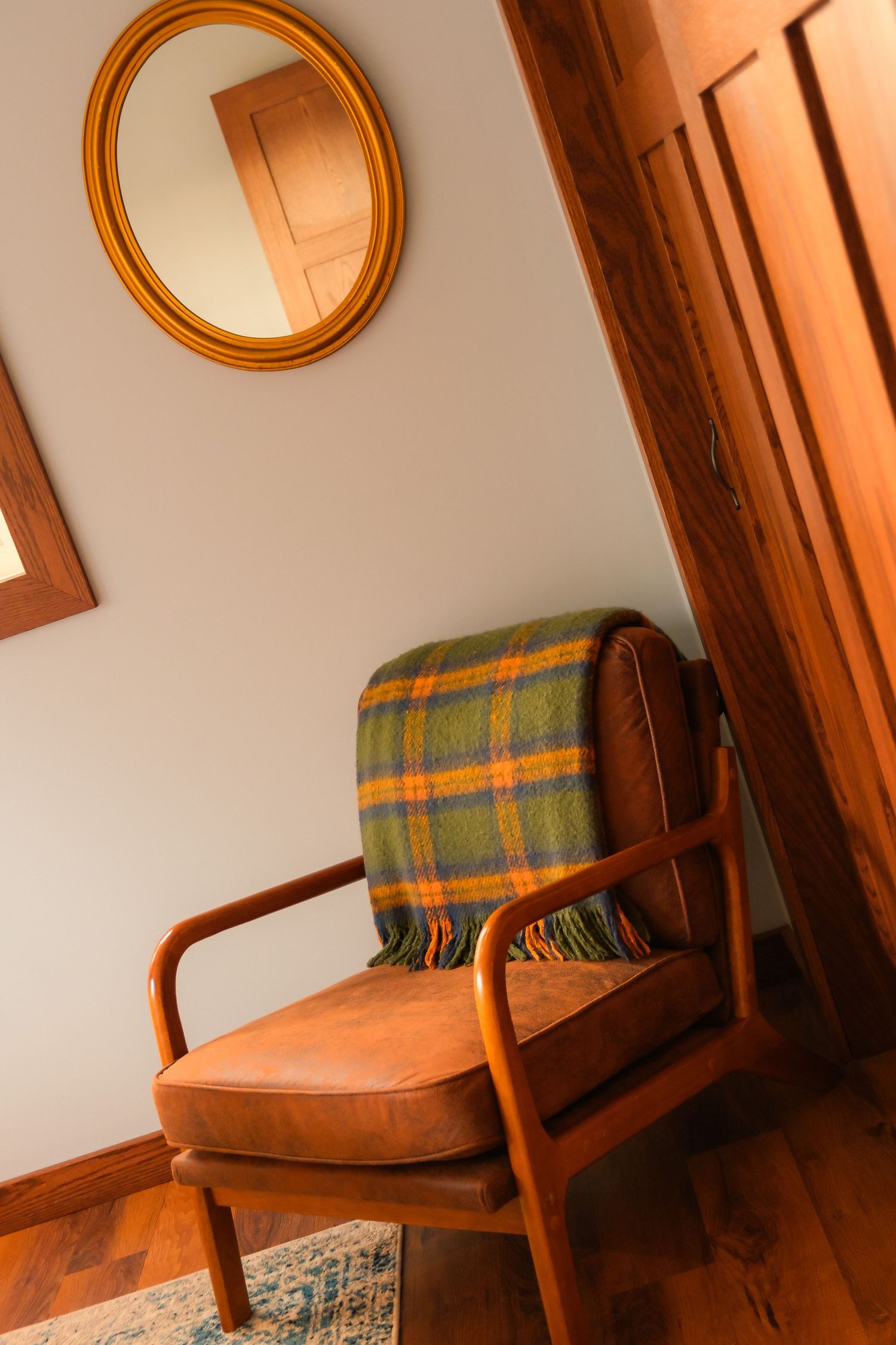 Mid-century modern armchair with plaid throw blanket beside circular mirror in warm-lit room.