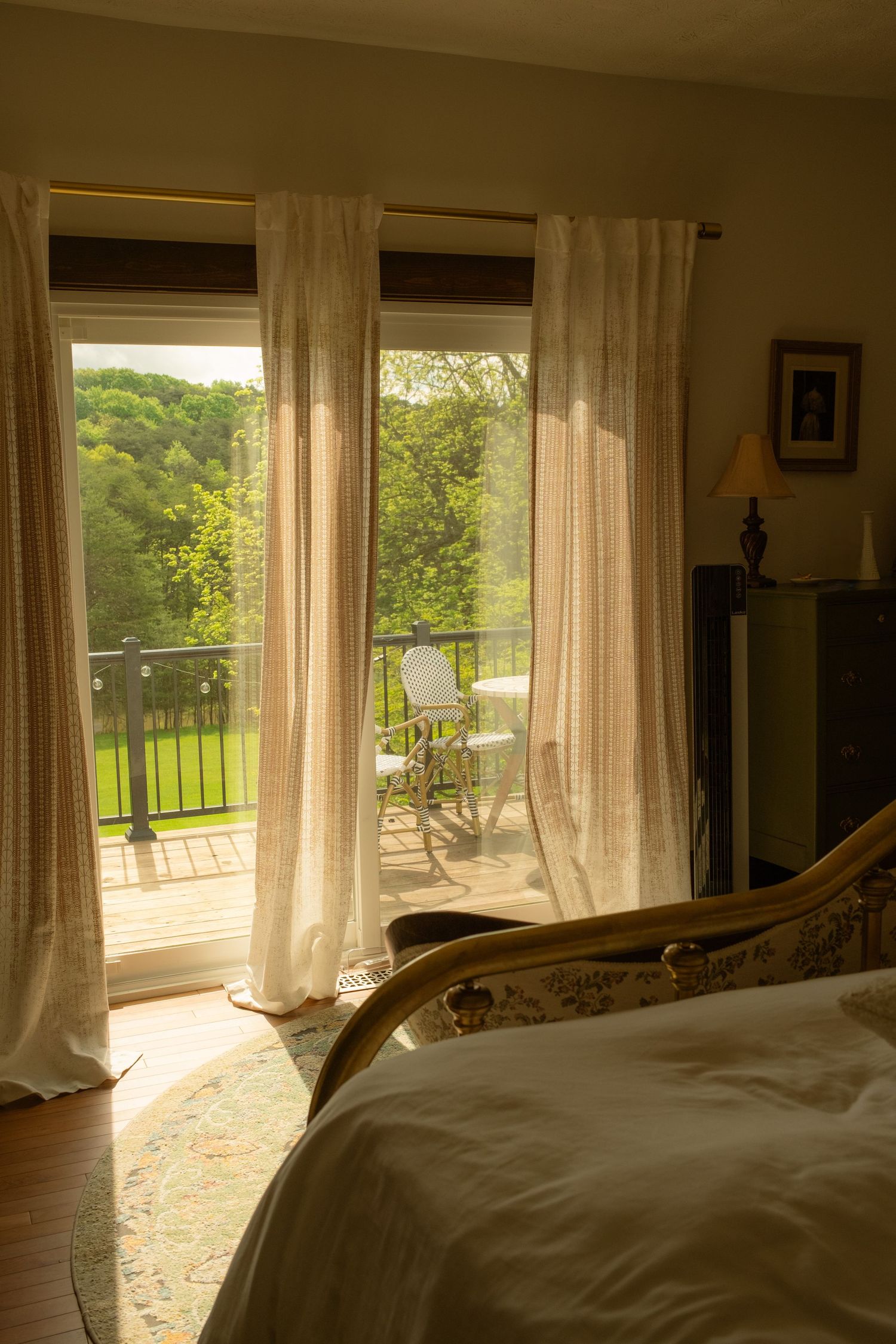 Sunlit bedroom with flowing white curtains and a view of green countryside.