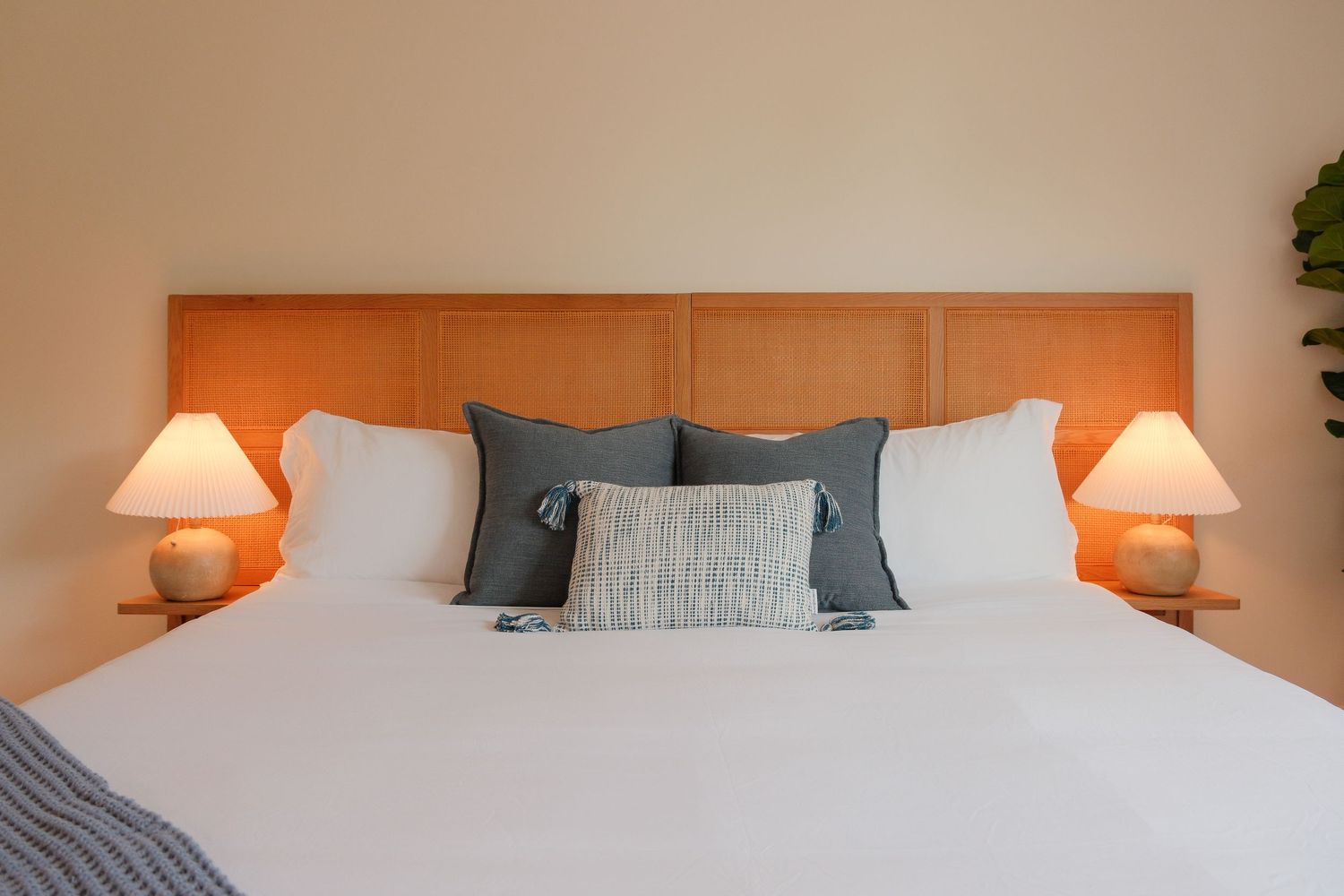 Elegant bedroom with a wooden headboard, white bedding, gray pillows, and warm bedside lamps on a neutral background.