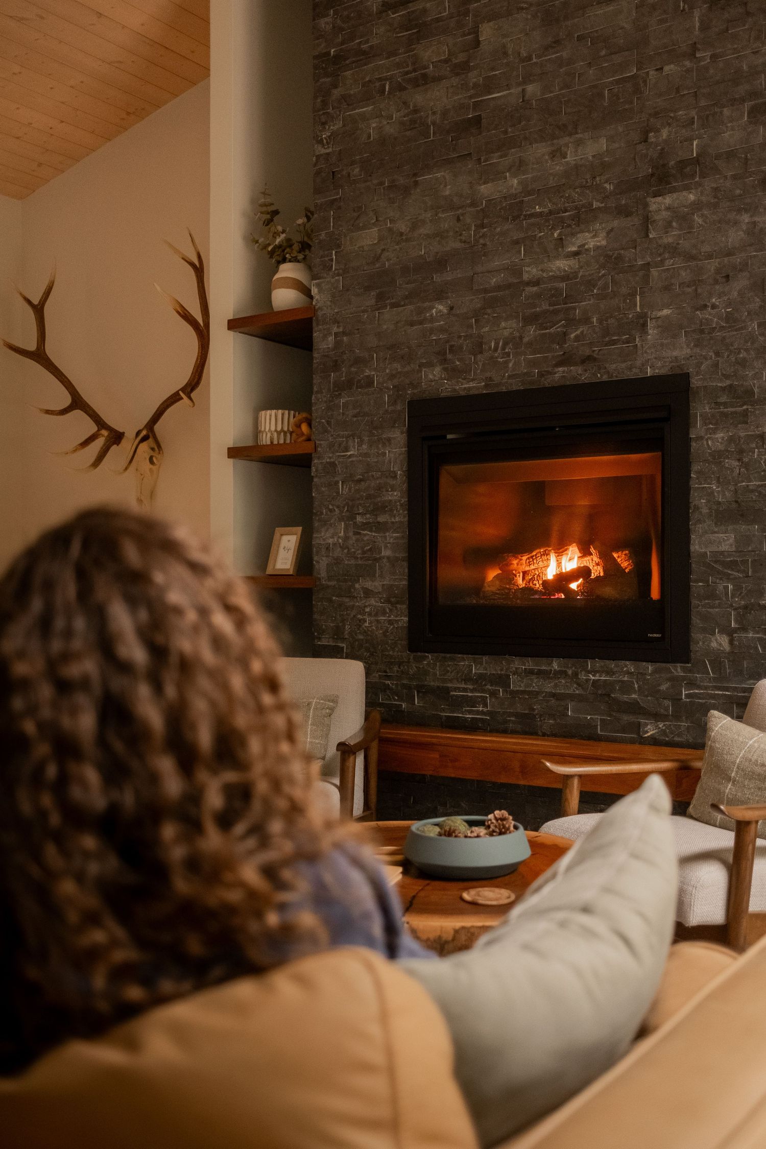 Warm fireplace glow illuminates stone accent wall with antler decor in modern cabin setting.