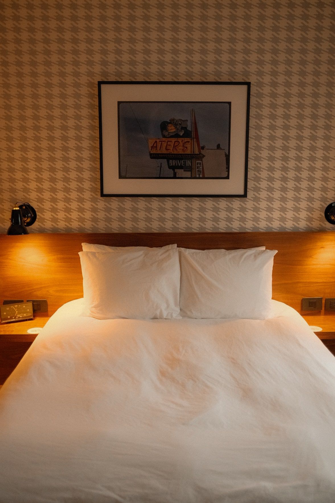 Contemporary hotel bed with crisp white linens and houndstooth pattern wallpaper.