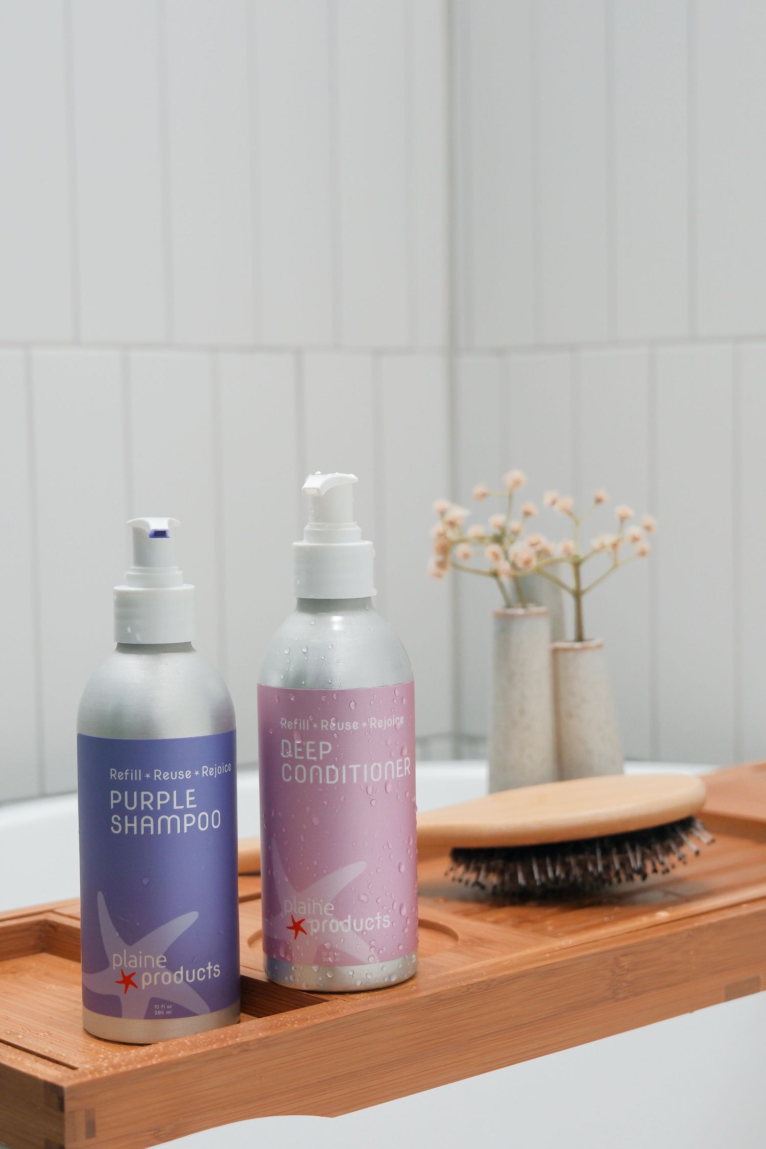 Plain Products Purple Shampoo and Deep Conditioner bottles on wooden bath tray with hairbrush.