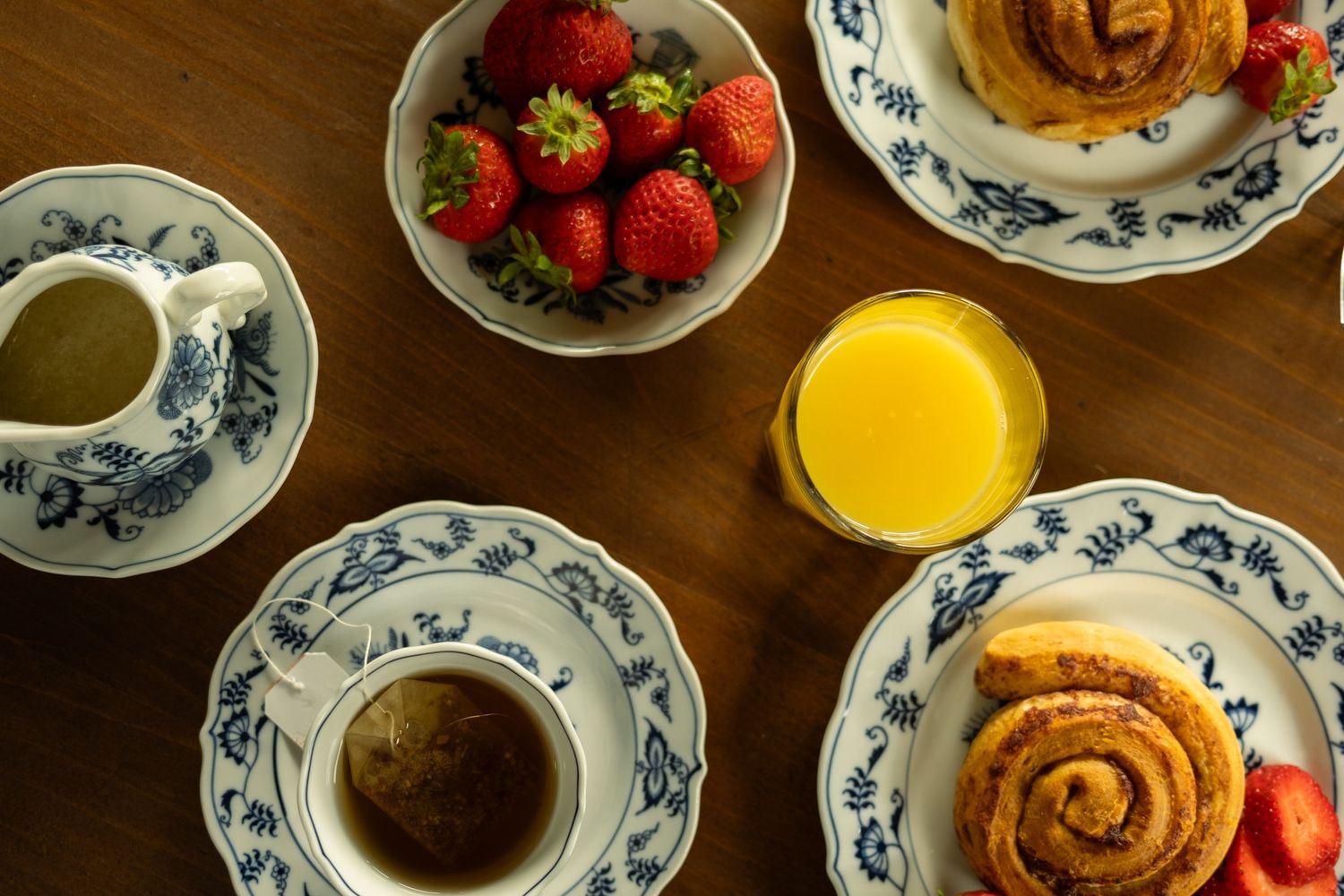 Breakfast spread of pastries and fresh fruit on decorative china plates with a glass of juice.