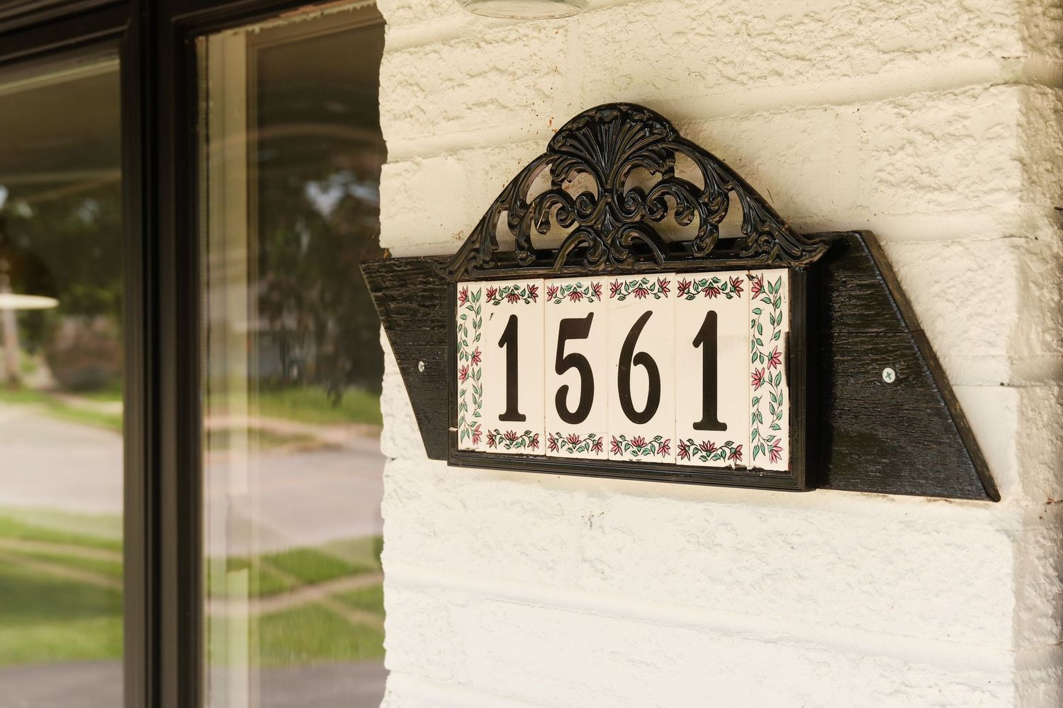 Decorative house number 1561 plaque with floral design mounted on white brick exterior wall near front door.