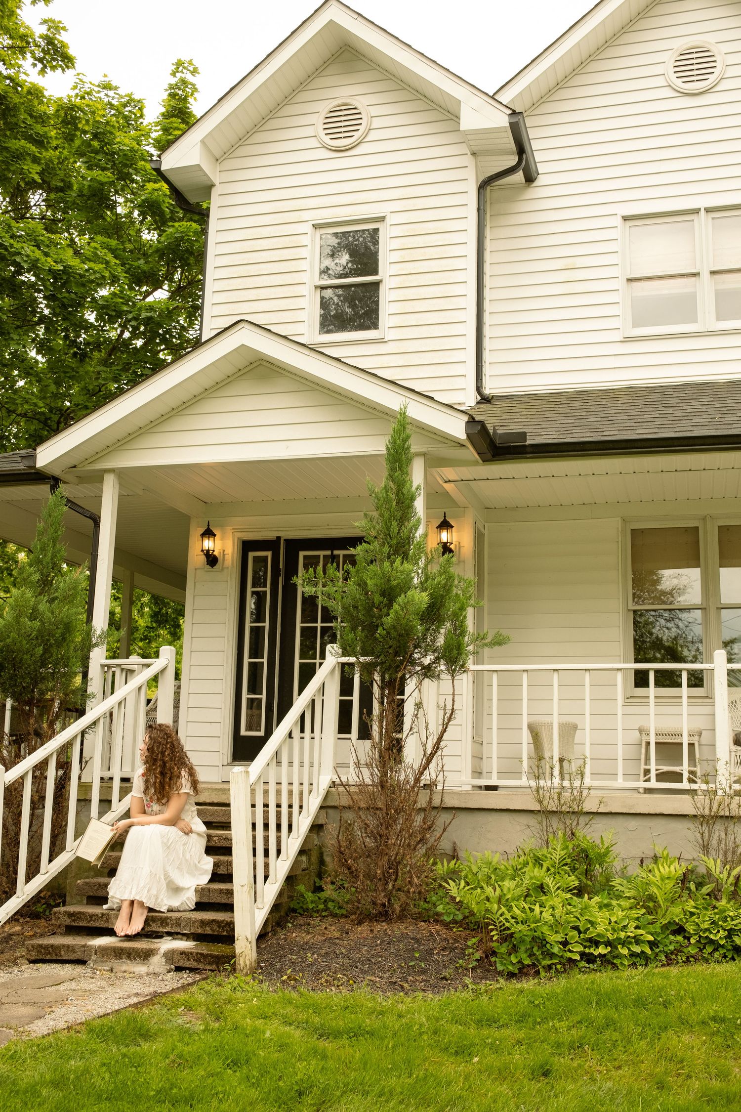 White farmhouse style home with wrap-around porch and landscaped garden.