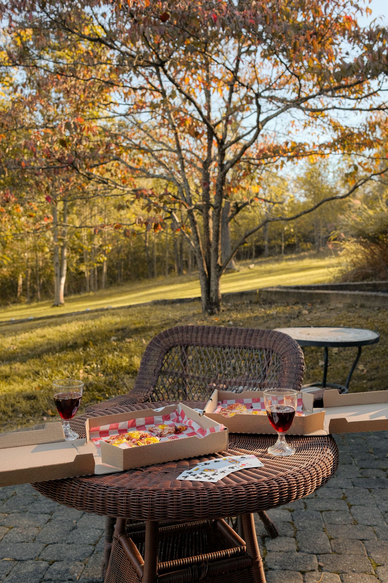 Outdoor dining setup with pizza and wine against autumn trees during golden hour.