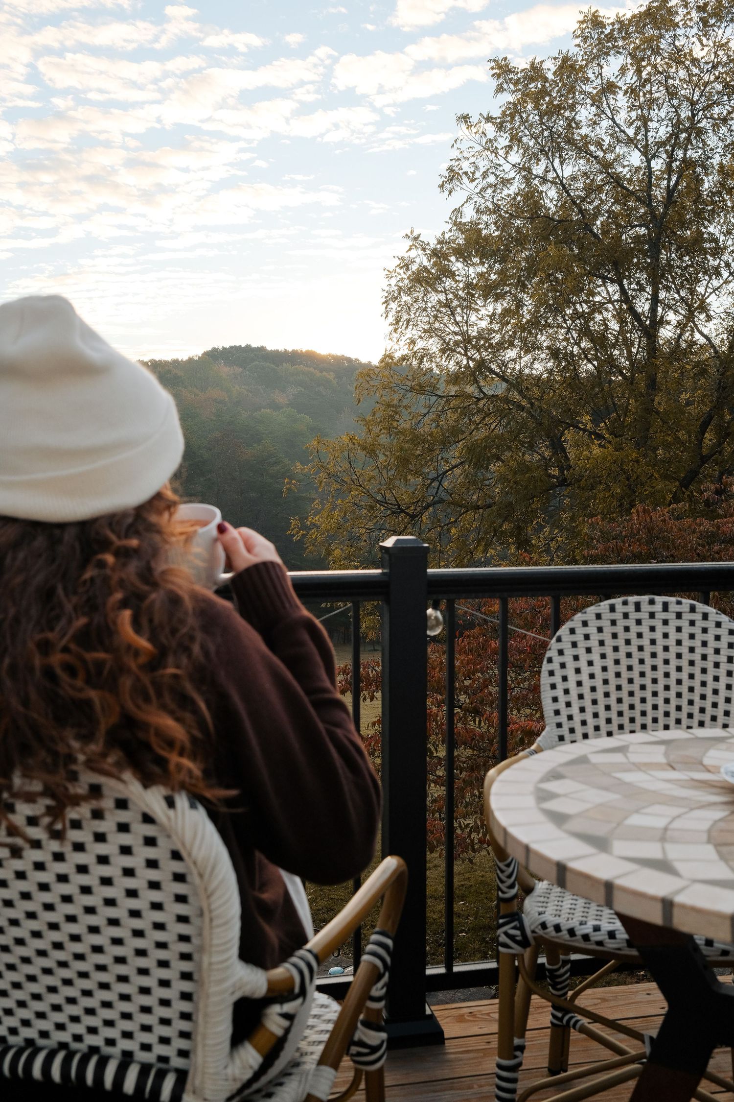 Person enjoying morning coffee on balcony overlooking autumn mountain landscape.