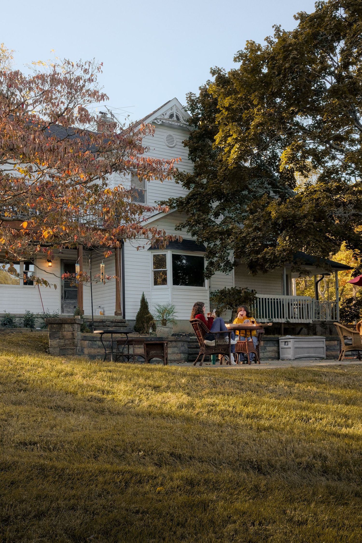 White farmhouse with porch seating area surrounded by autumn foliage at sunset.