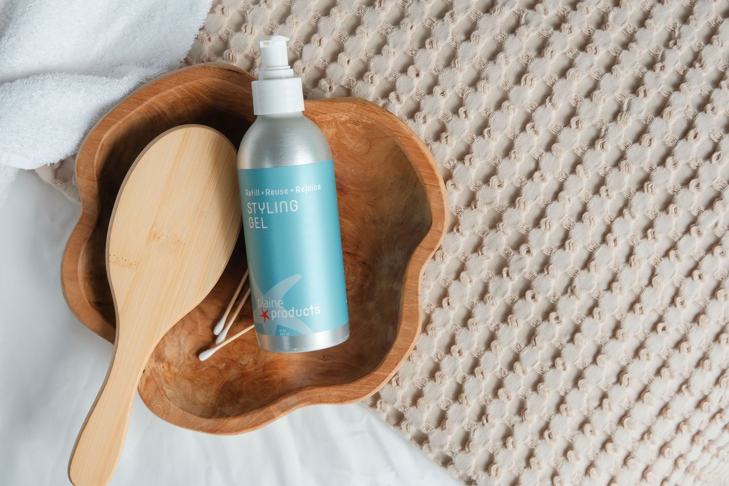 Wooden bowl with a hair brush and blue styling gel bottle on a textured cream surface.