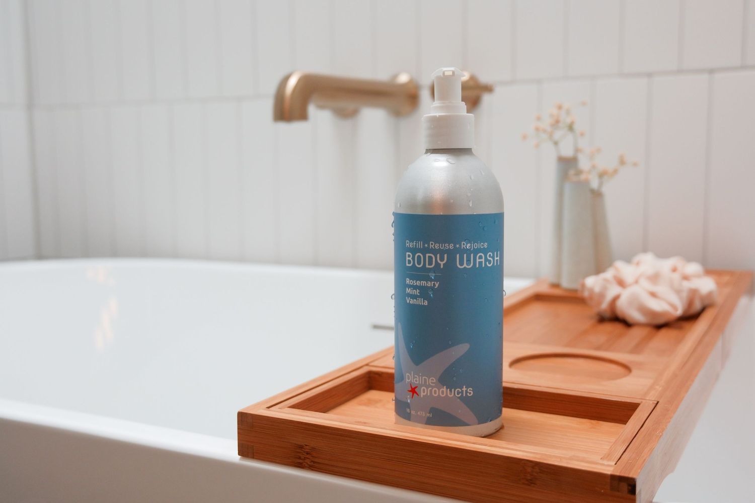 Arctic freeze mineral body wash bottle on a wooden bath tray beside a white bathtub with gold faucet.