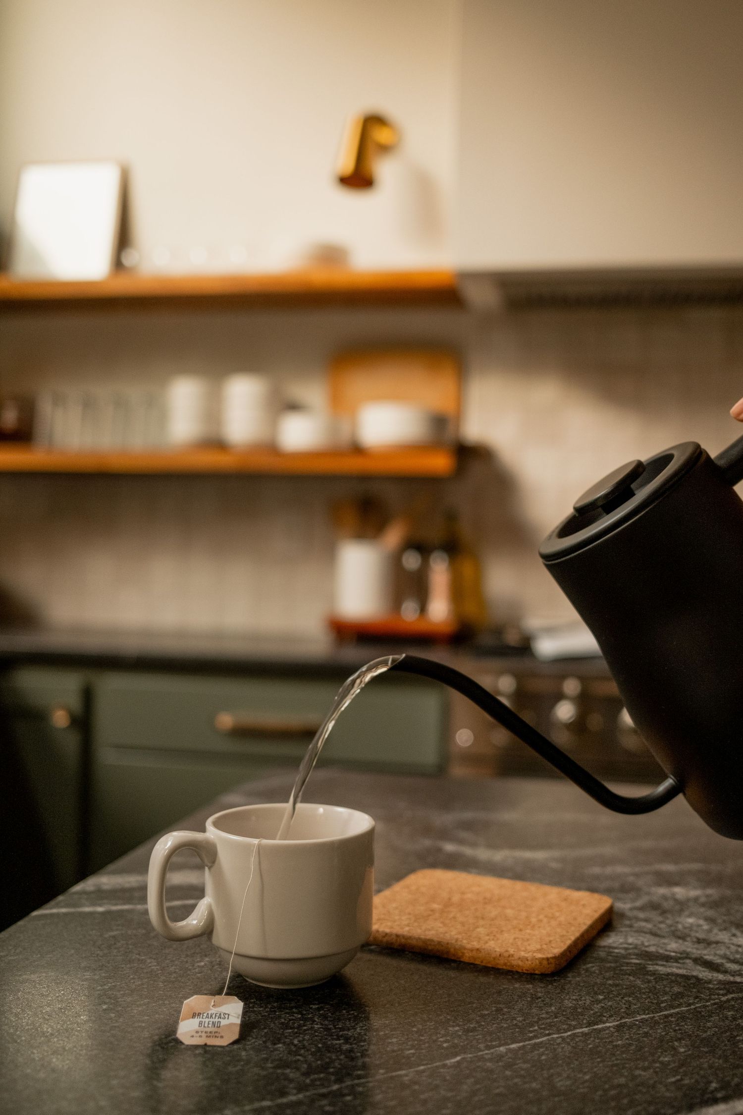 Tea being poured into a white ceramic cup on a dark countertop with morning light.