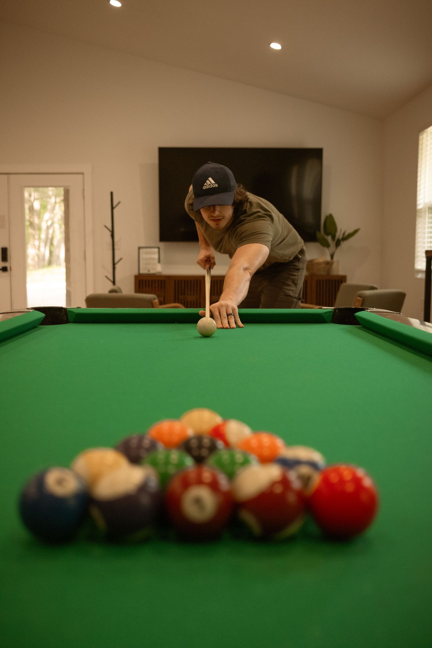 Person in casual attire lining up a shot on a green pool table with racked balls.