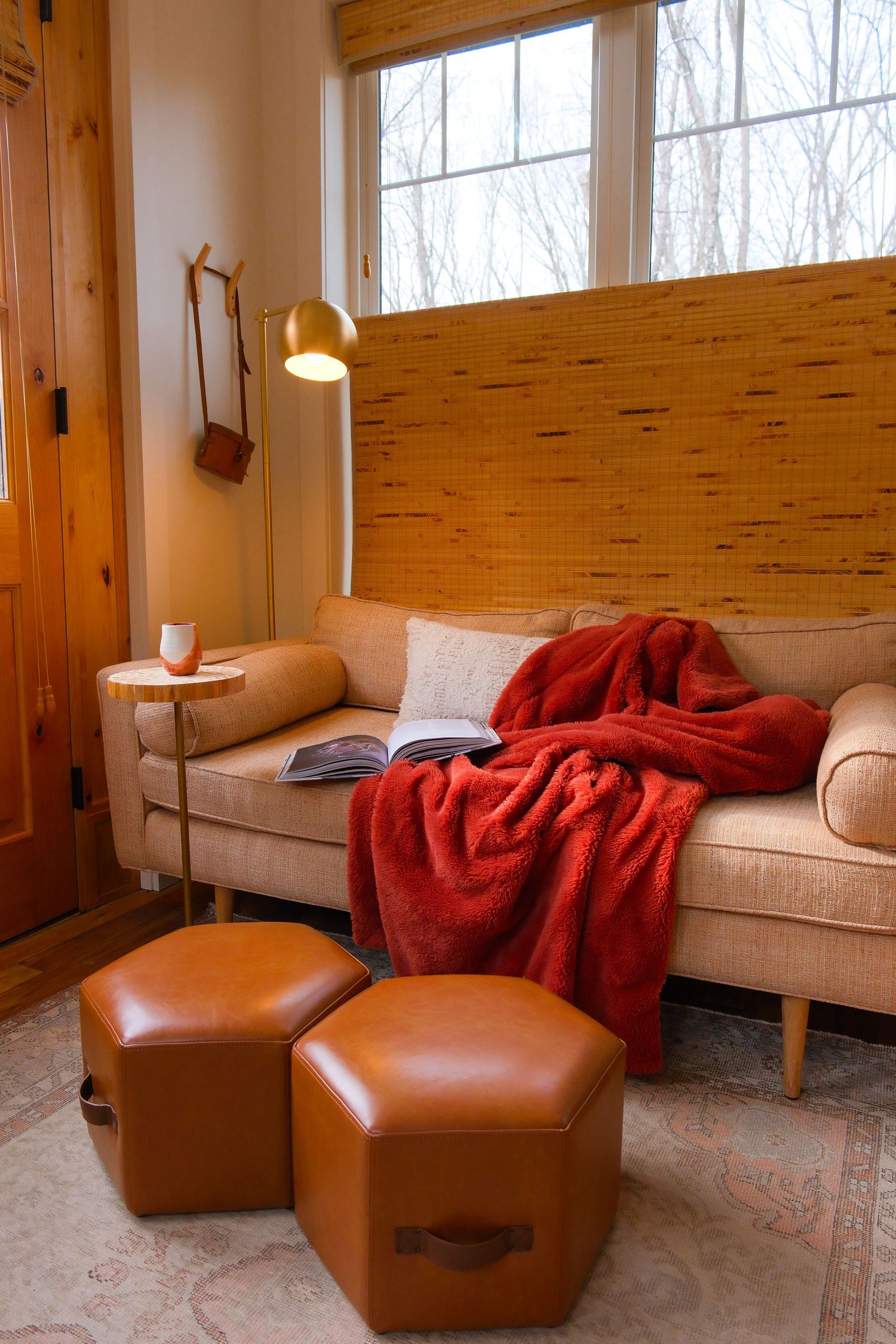 Warm living room with beige sofa, red throw blanket, leather ottomans, and a gold floor lamp.