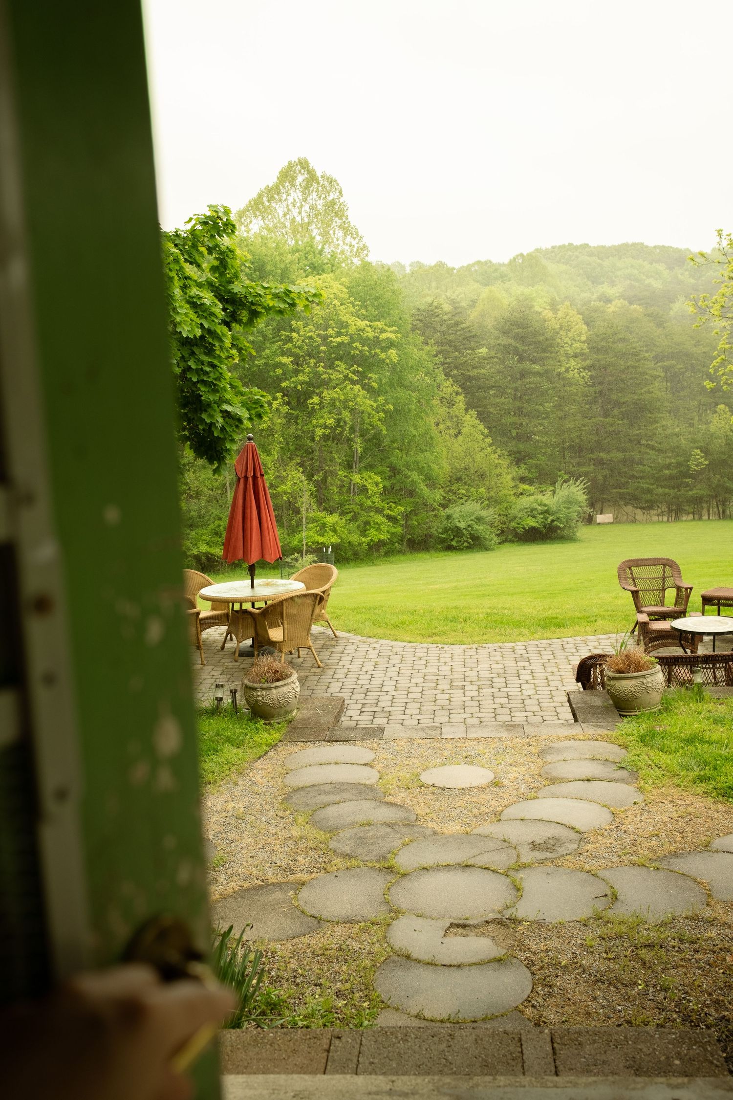 Stone patio with circular pavers leads to a lush green lawn with outdoor furniture.