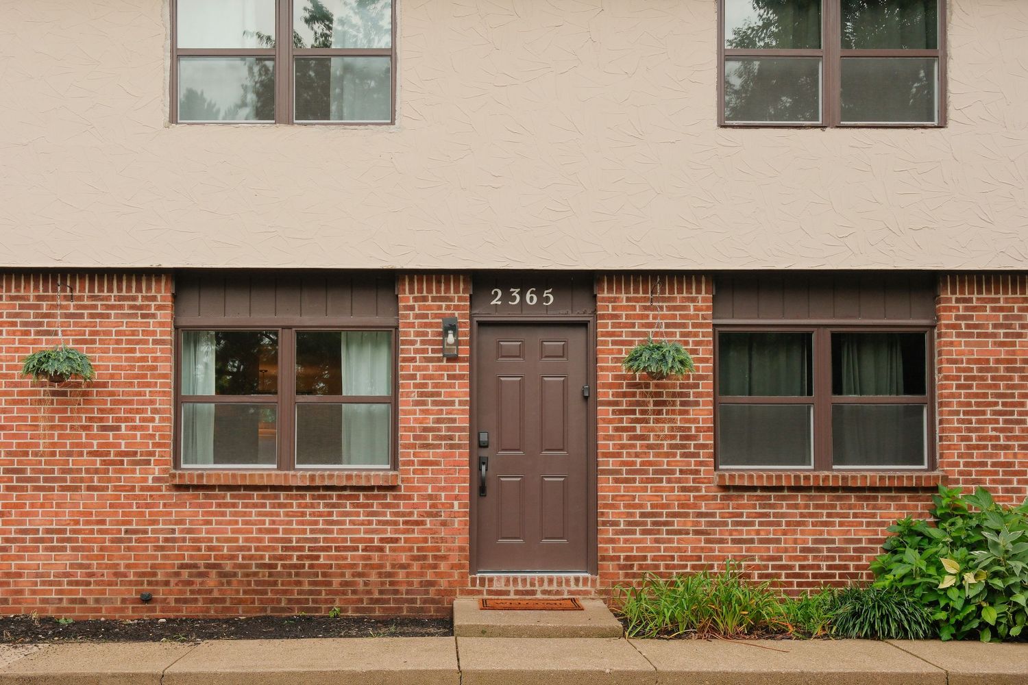 Brick townhome exterior at 2365 featuring a brown front door, symmetrical windows with flower boxes, and manicured landscaping.