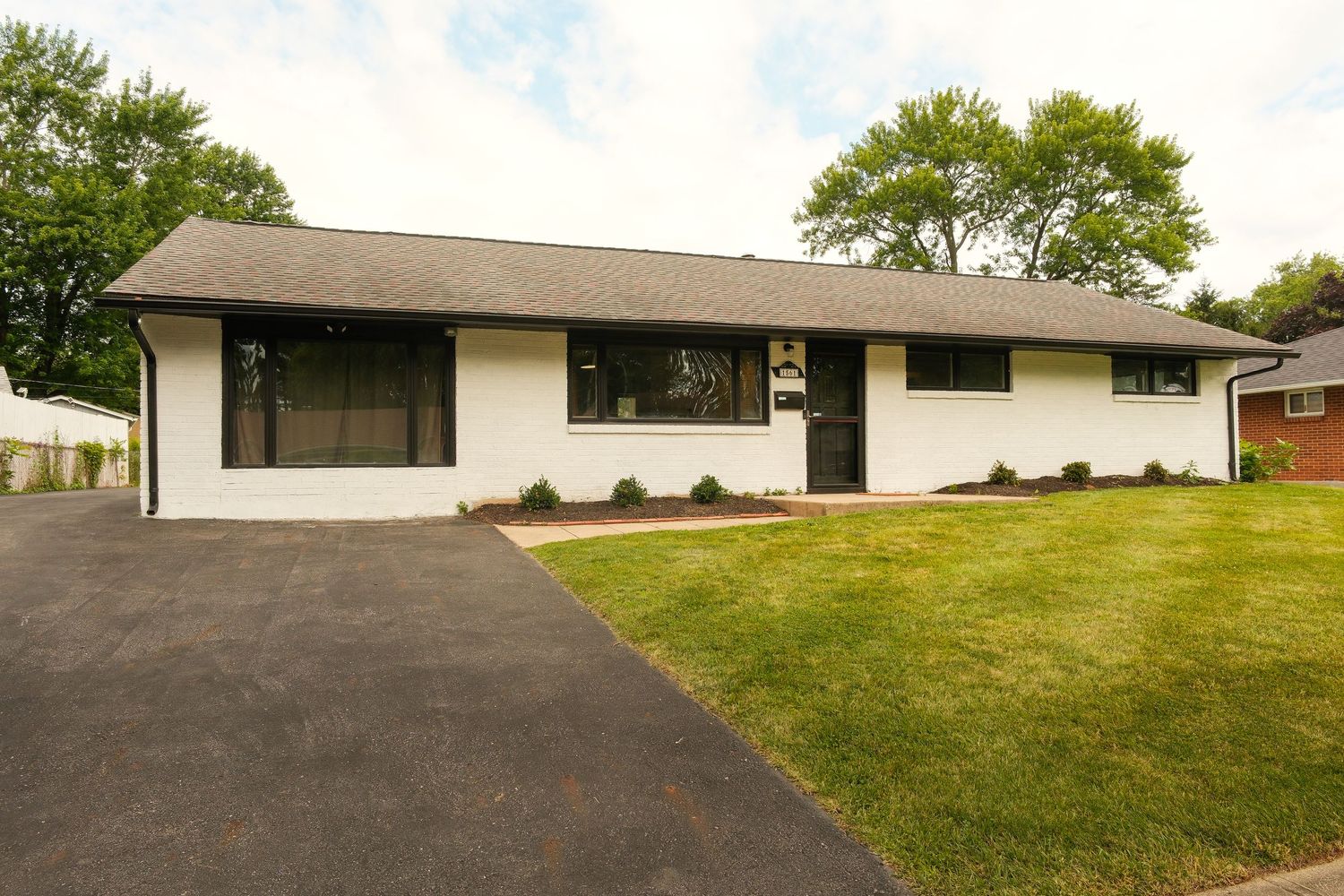 White ranch-style home with black trim, attached garage, manicured lawn, and mature trees in a suburban neighborhood.