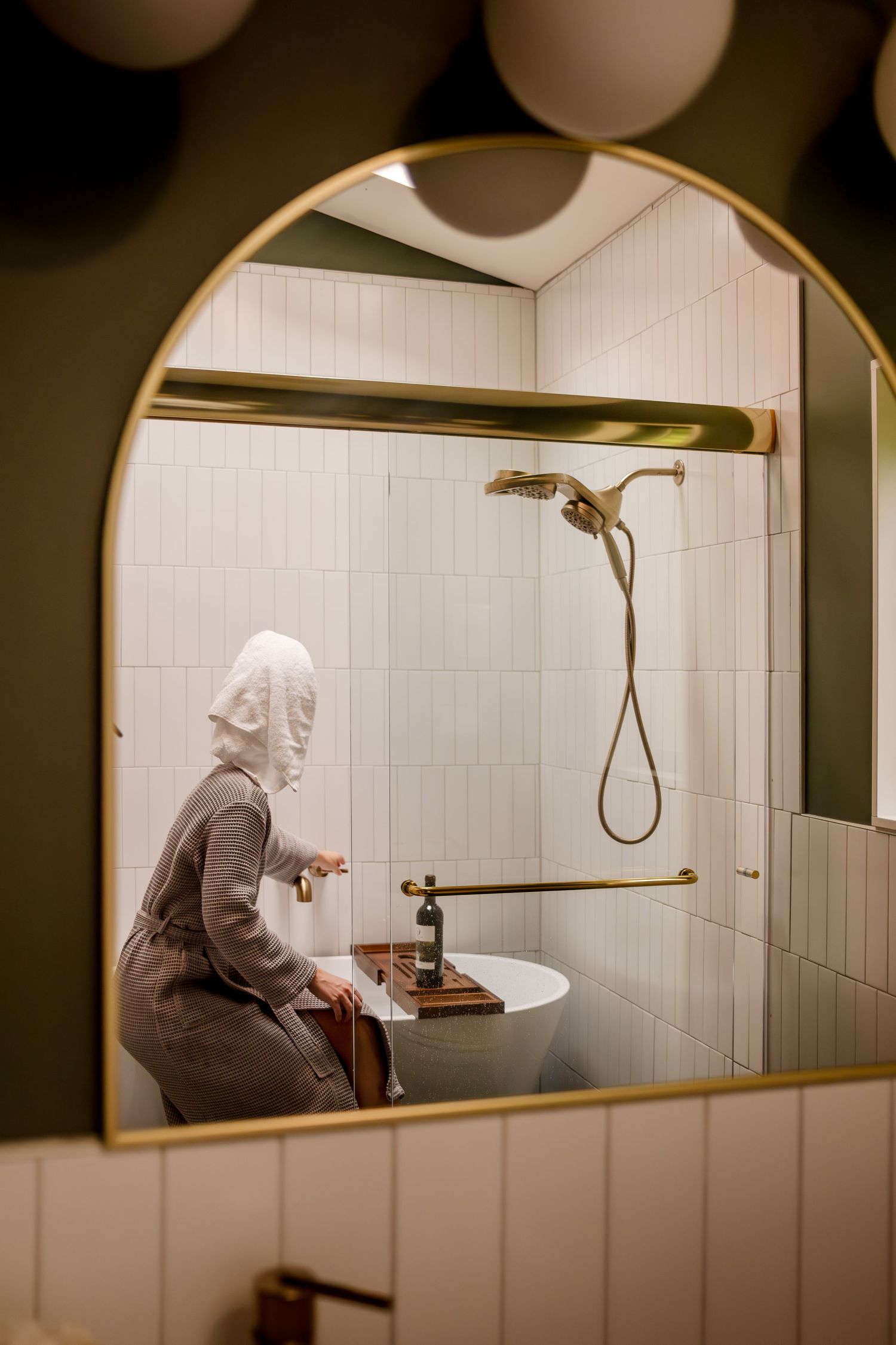 White tiled bathroom interior with arched mirror and gold fixtures.