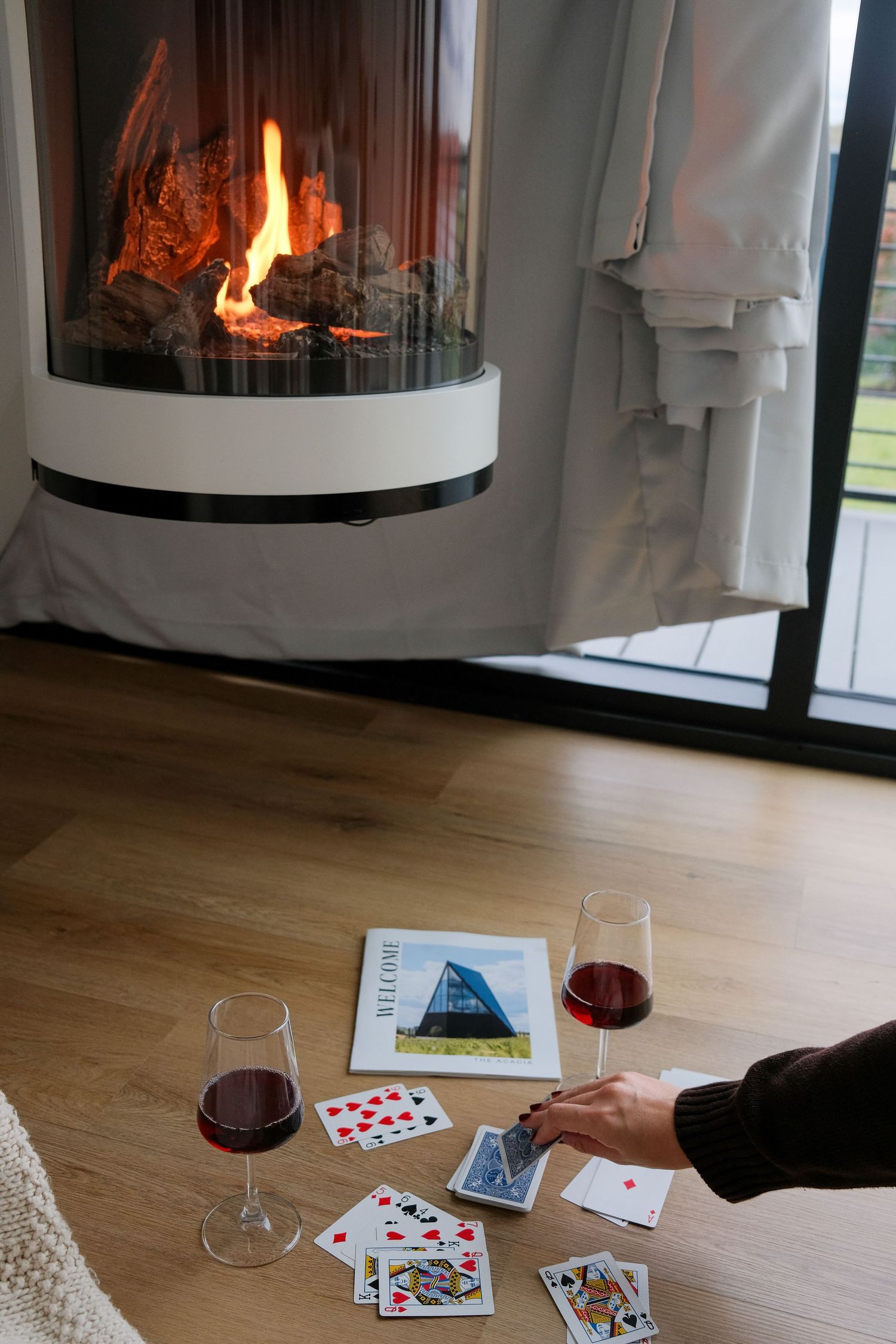 Playing cards and wine glasses arranged near a modern fireplace with flames visible.